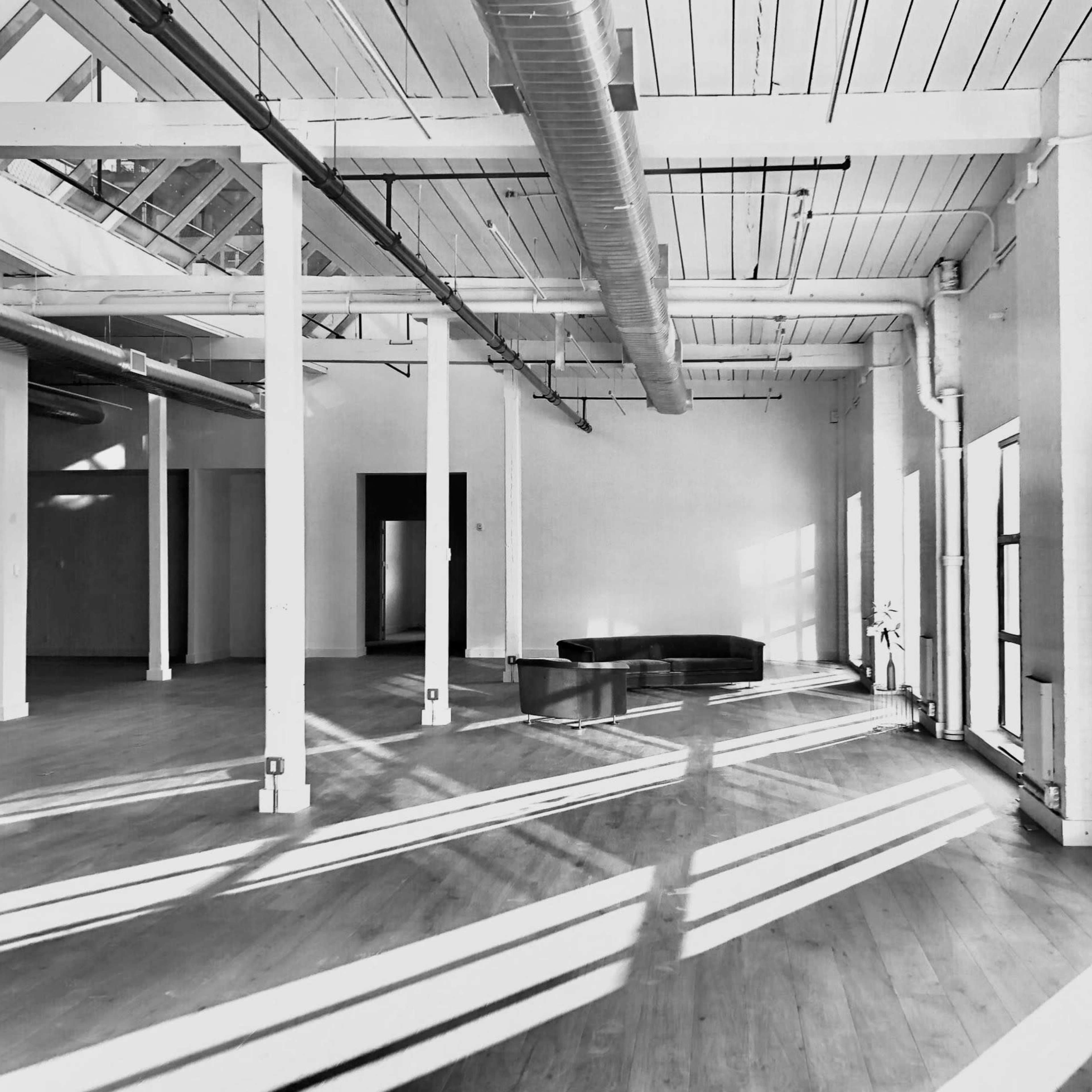 An empty, well-lit industrial space with wooden flooring, large windows, and metal support columns.