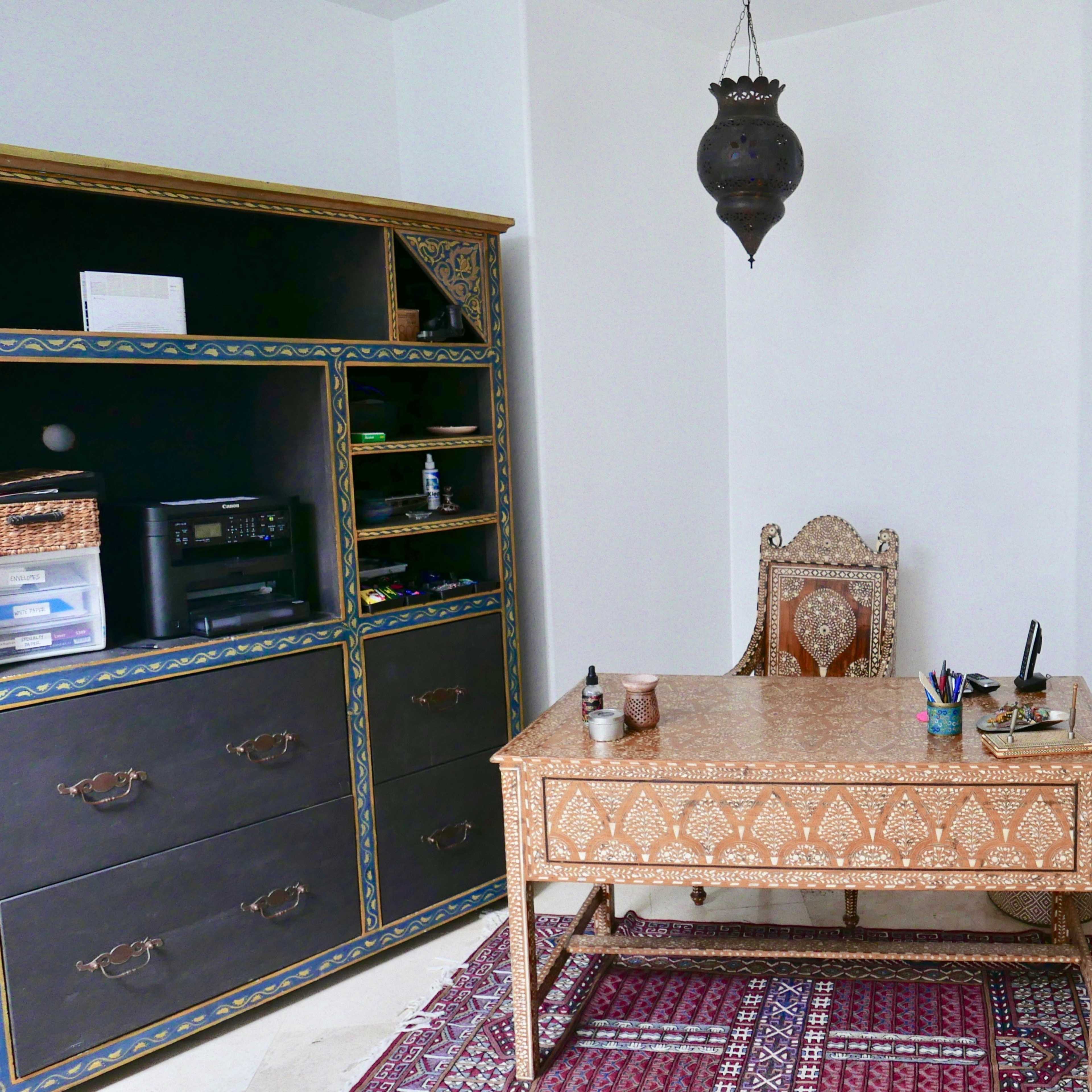 A well-decorated room featuring a wooden desk, an intricately designed chair, a storage unit, and a carved wooden door.