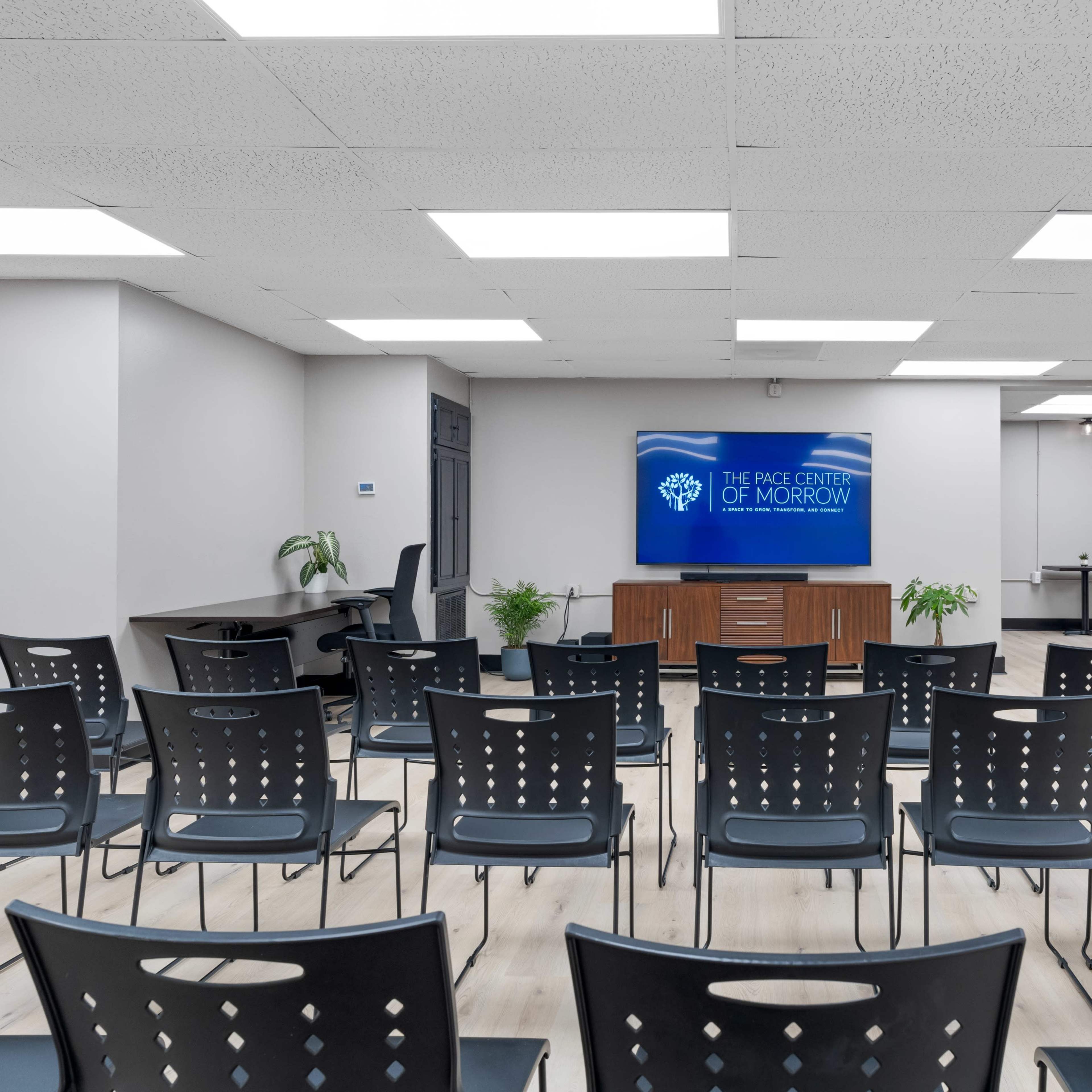 A conference room with rows of black chairs facing a wall-mounted display screen that reads "THE PACE CENTER OF MORROW."