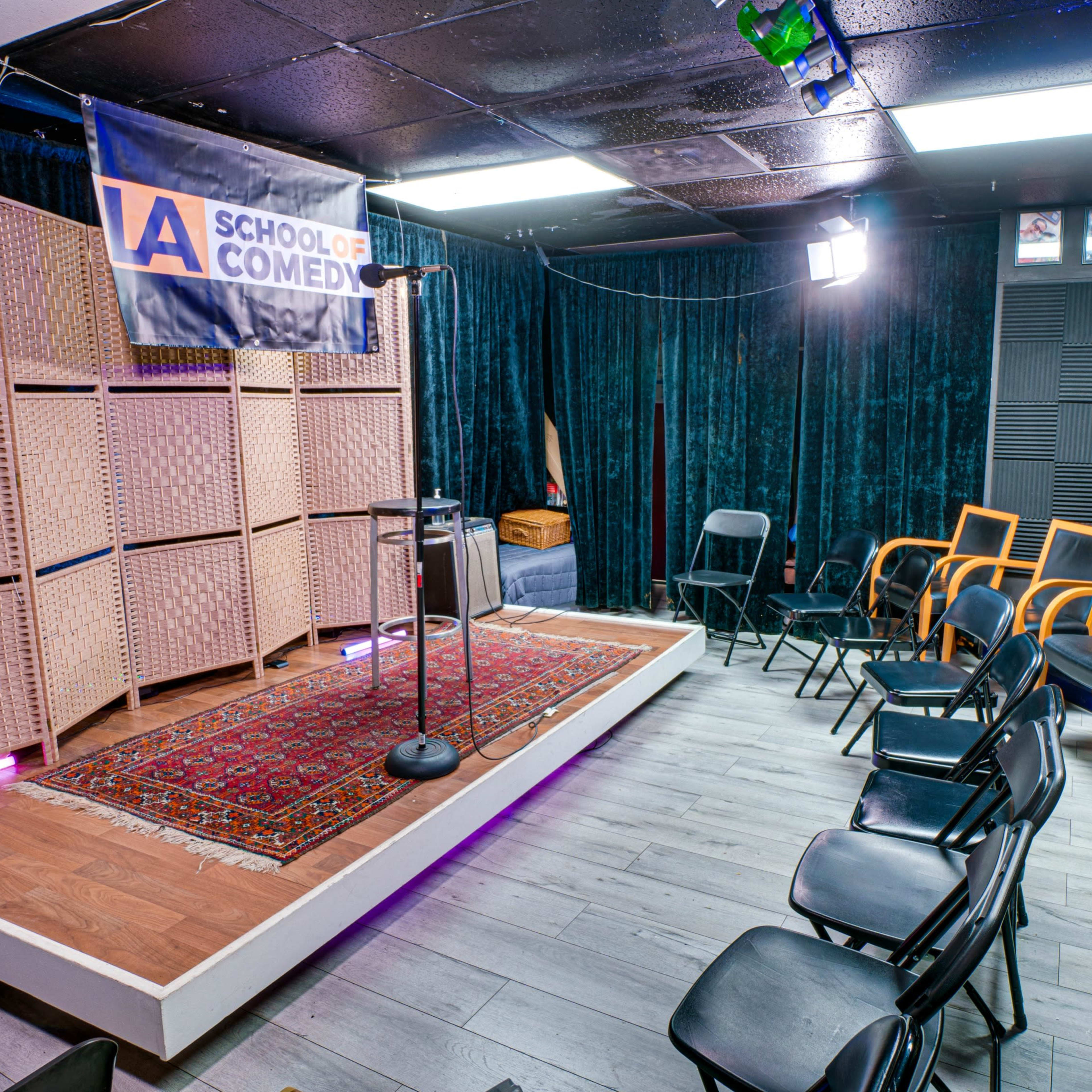 A comedy performance stage with a microphone stand, surrounded by seating arranged in a semi-circle.