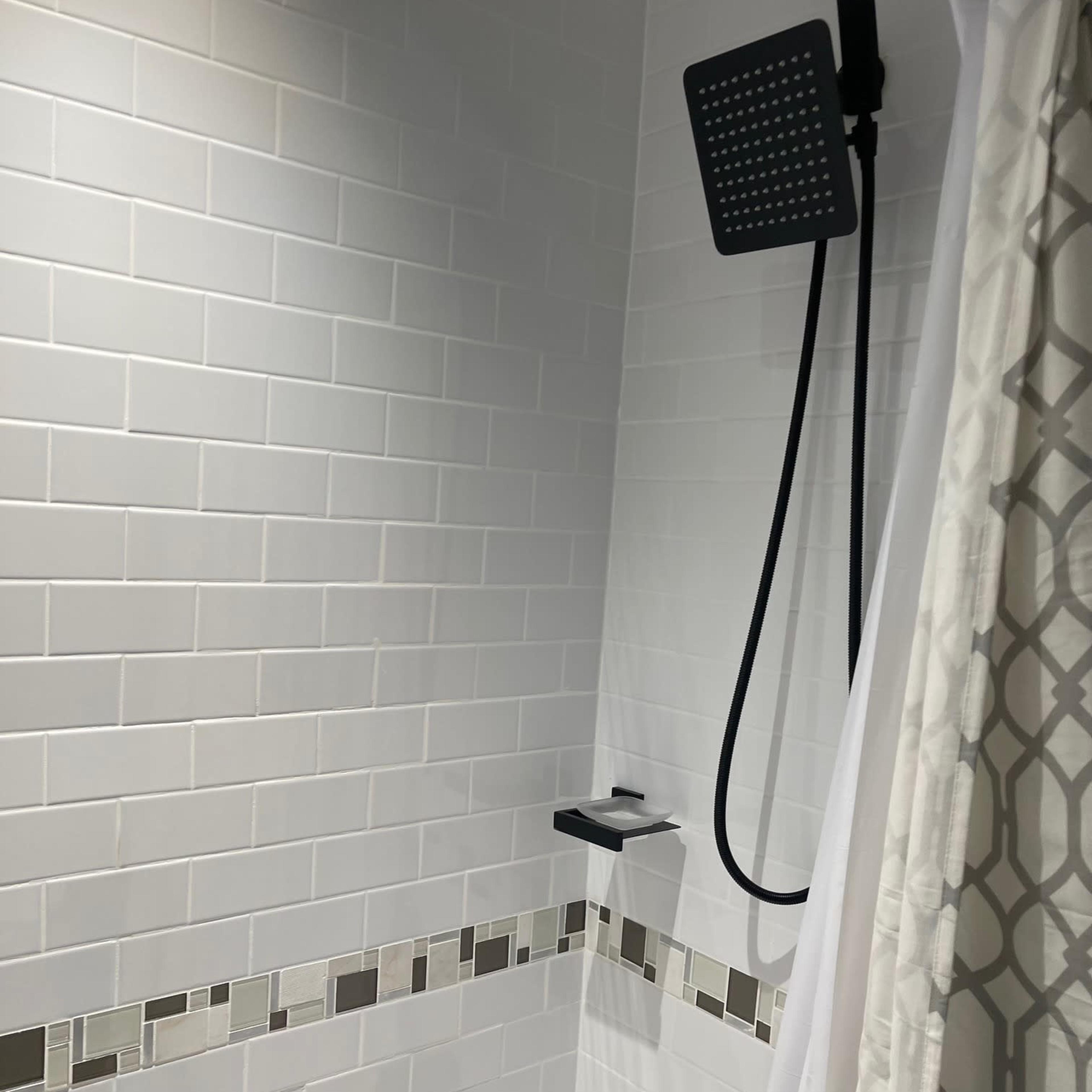 A modern shower with a large overhead showerhead, tiled walls, and a minimalist shelf for toiletries.