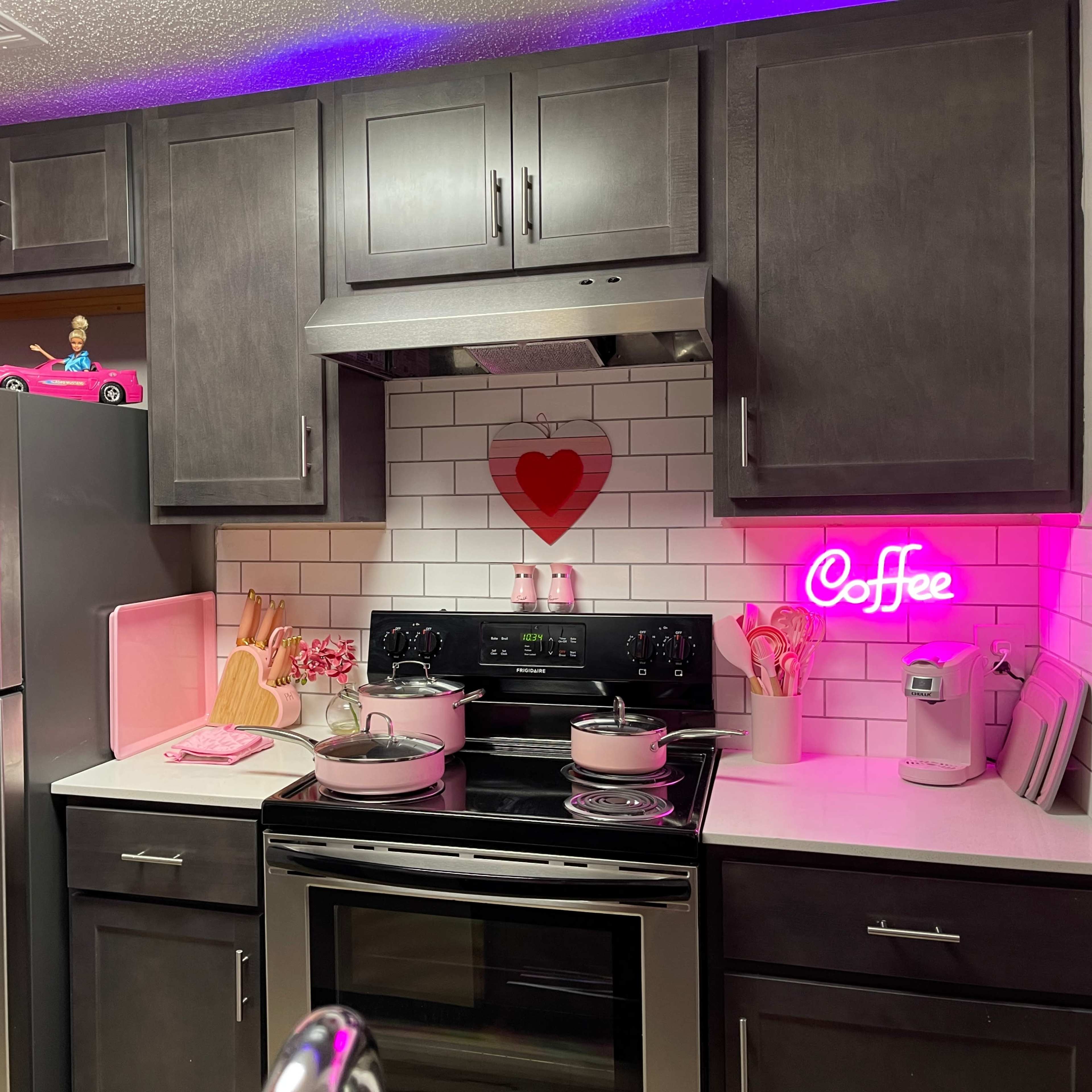 A modern kitchen features dark cabinetry, stainless steel appliances, and a decorative pink heart and neon "Coffee" sign on the walls.