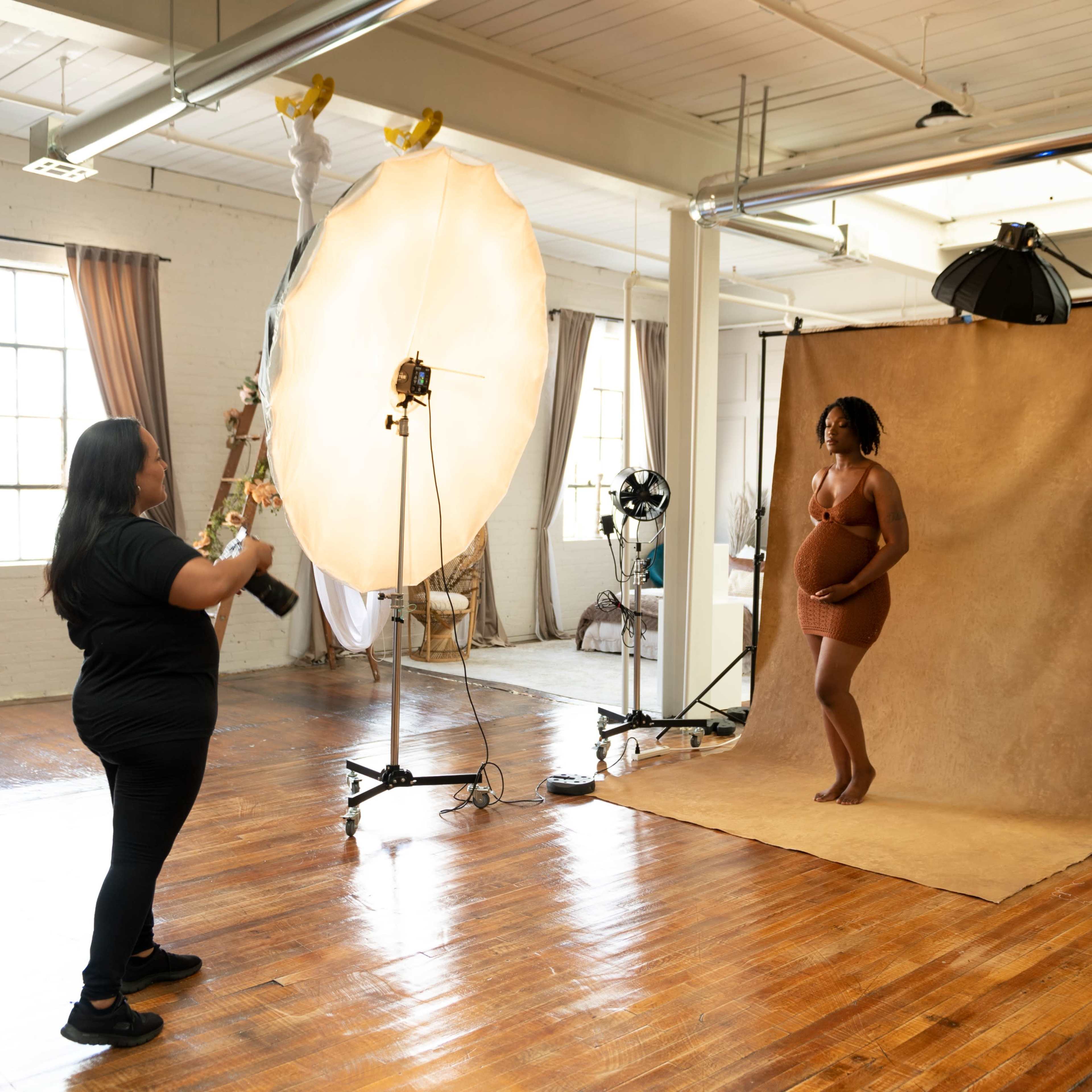 A photographer captures a model posed with a large round prop in a studio setting with soft lighting and backdrops.