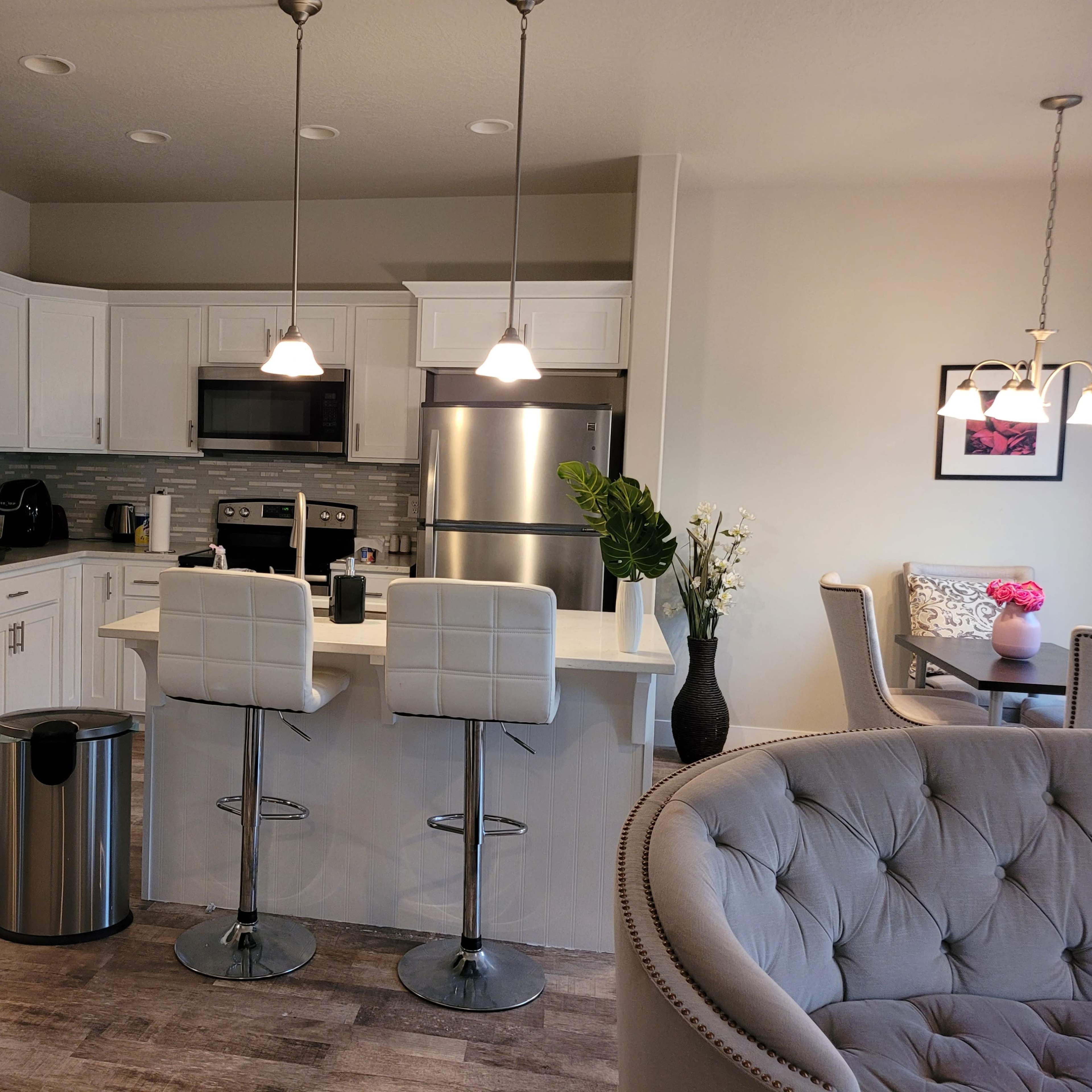 A modern kitchen with white cabinets, stainless steel appliances, and a breakfast bar with two stools.