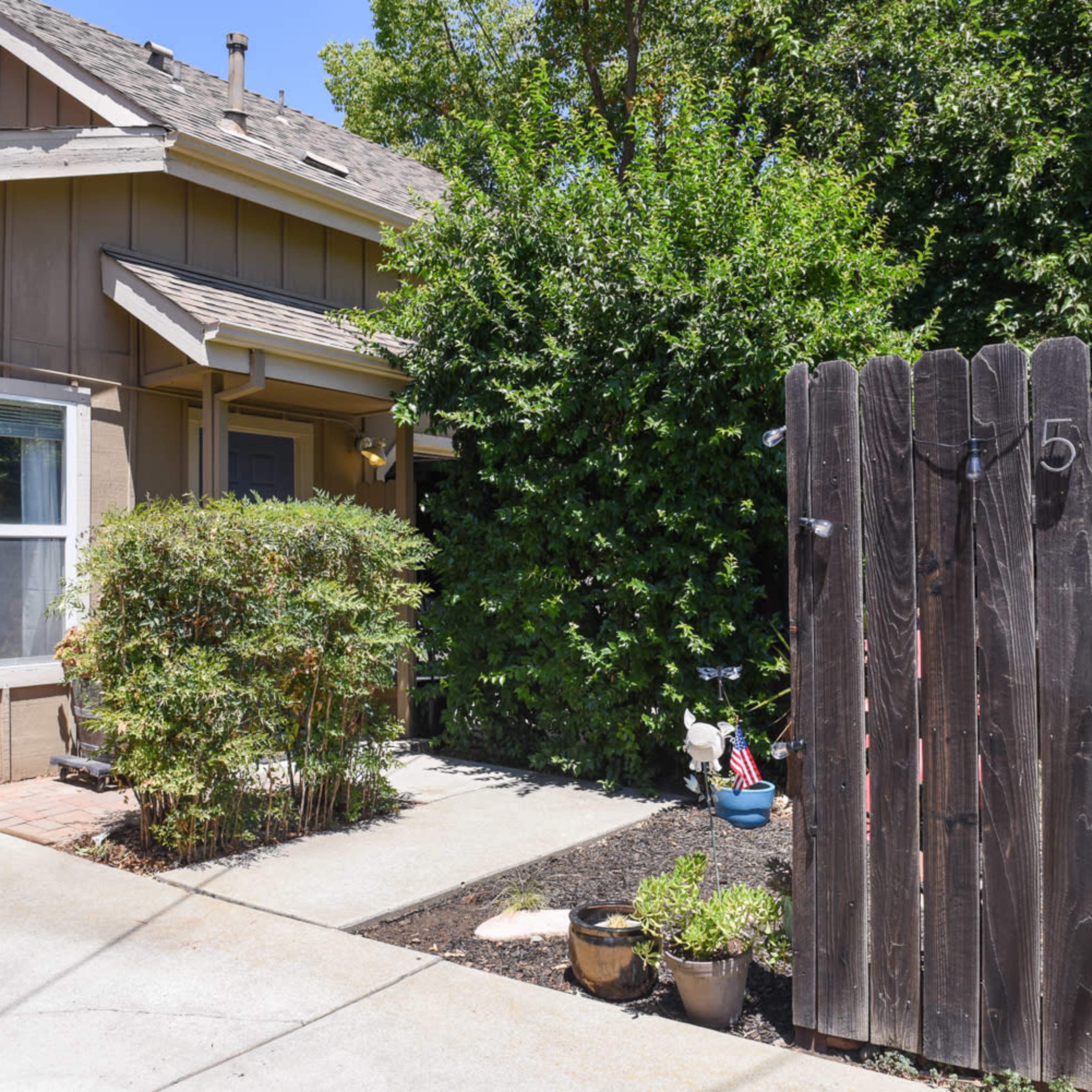 A brown wooden fence with the number "509 B" stands beside a pathway leading to a house with a front porch and surrounding greenery.