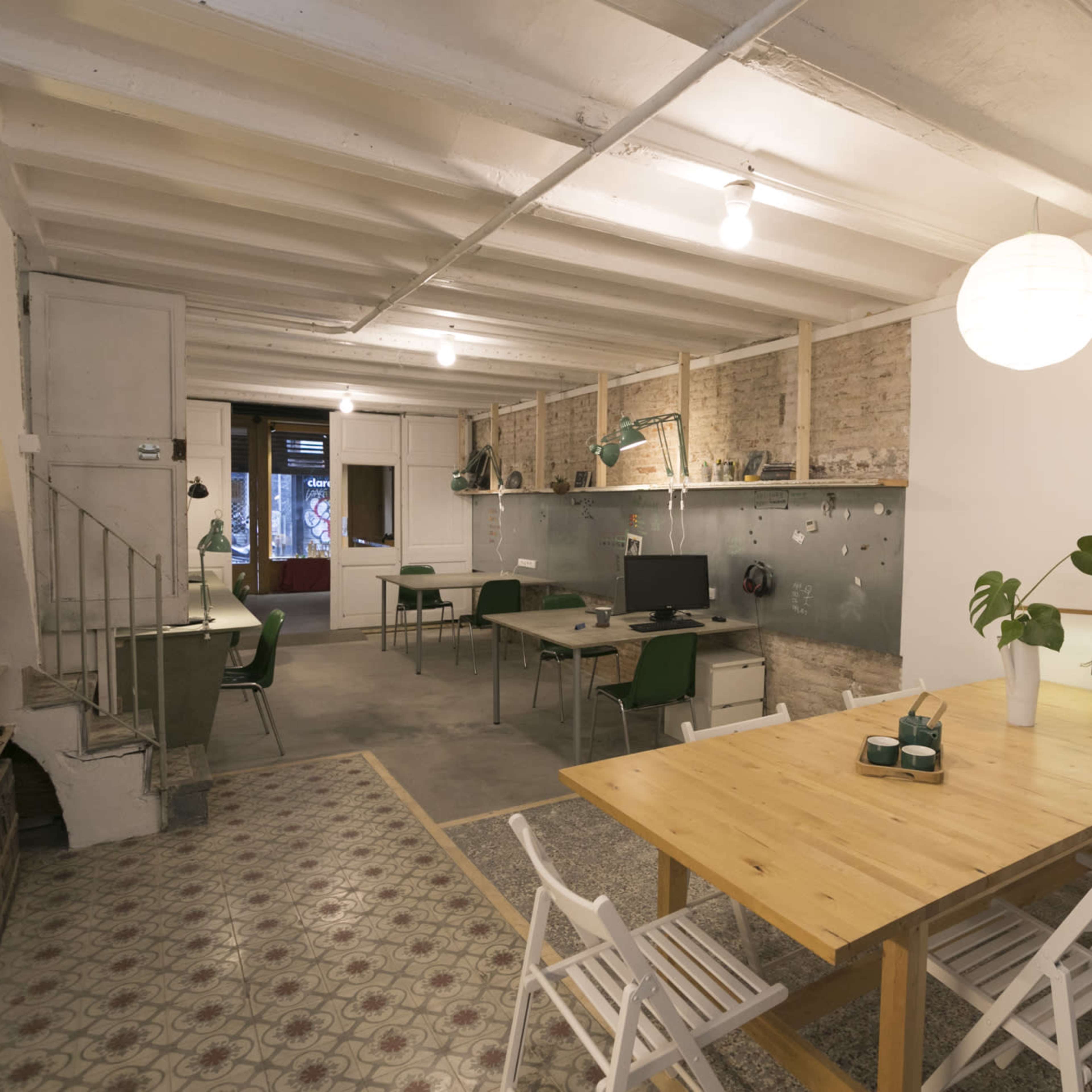 A spacious room with a dining area featuring wooden tables and chairs, a workspace with computers, and a minimalist design aesthetic.