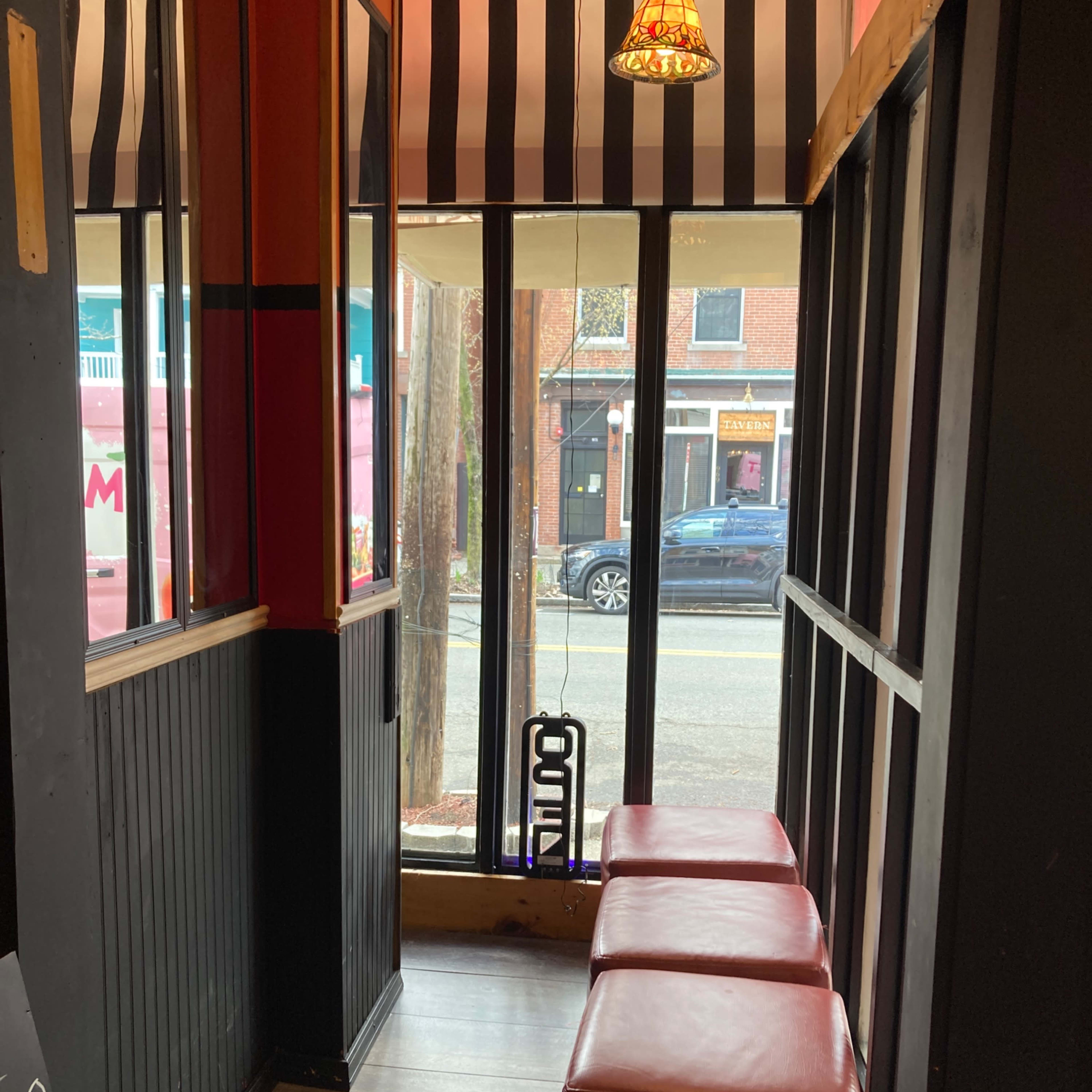 A small indoor seating area with two red benches and large windows facing a street lined with parked cars.