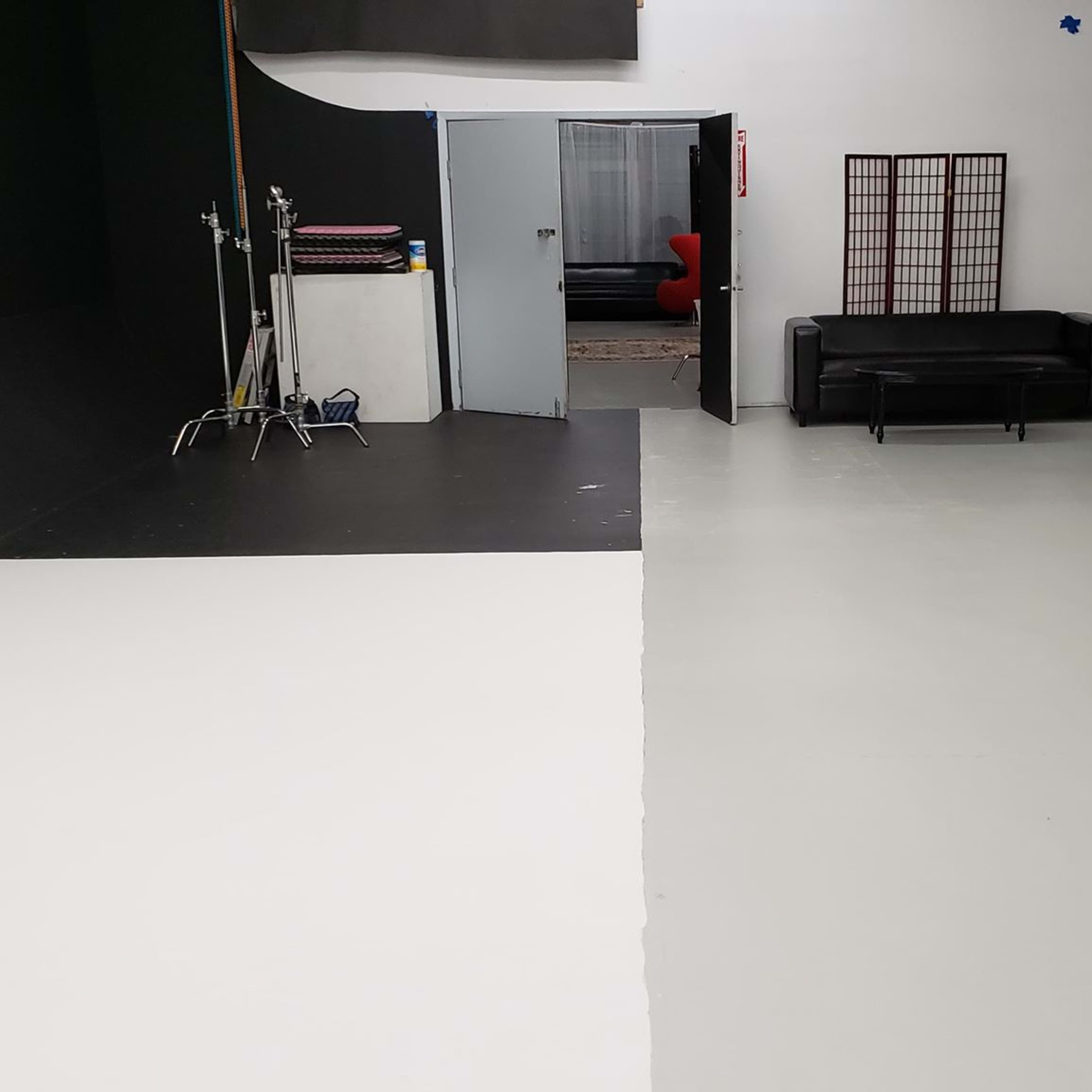 A photography studio with a divided floor featuring black and white sections, a doorway leading to another area, and various seating options including a black couch and an ornate chair.