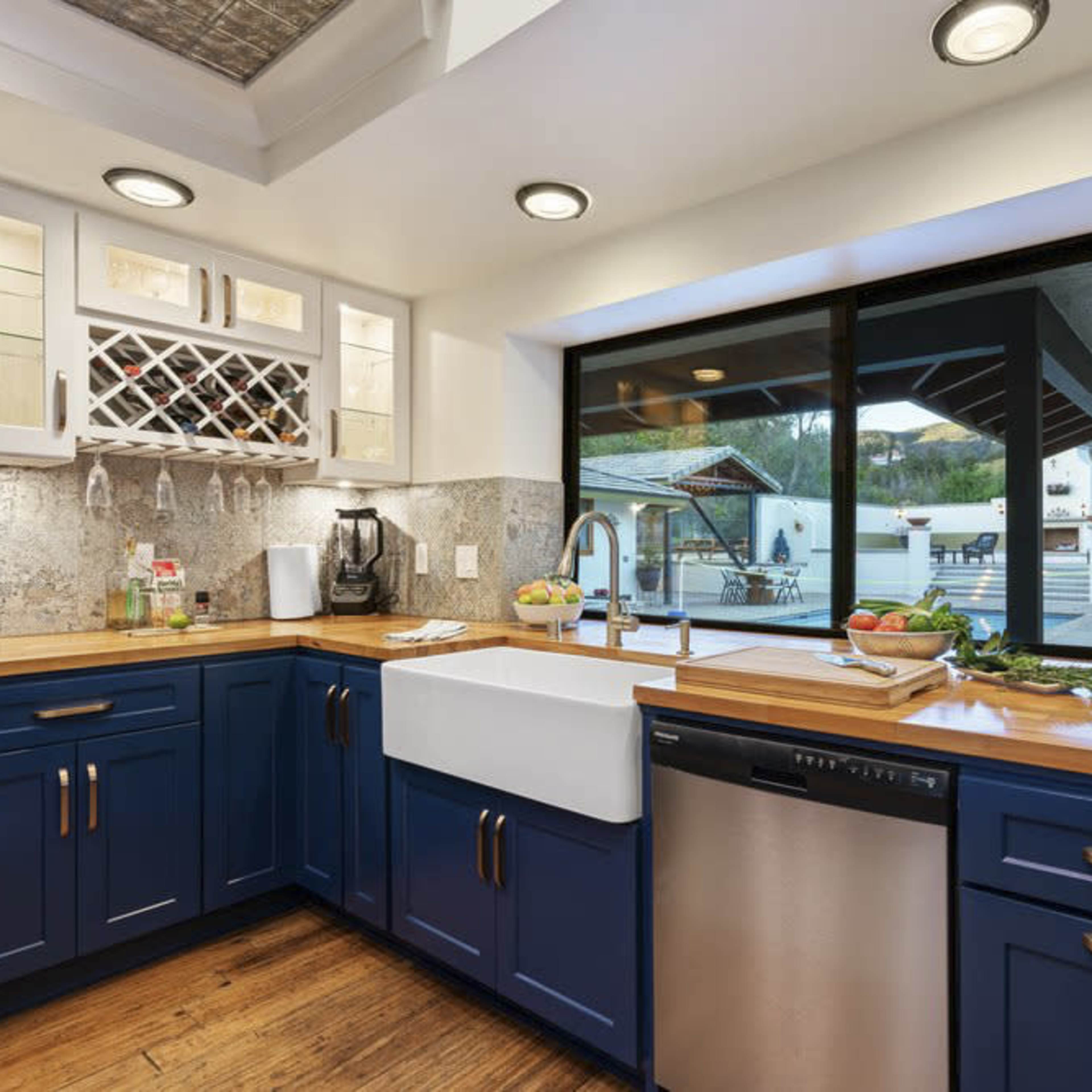 A modern kitchen with blue cabinets, a farmhouse sink, and a window overlooking an outdoor patio area.