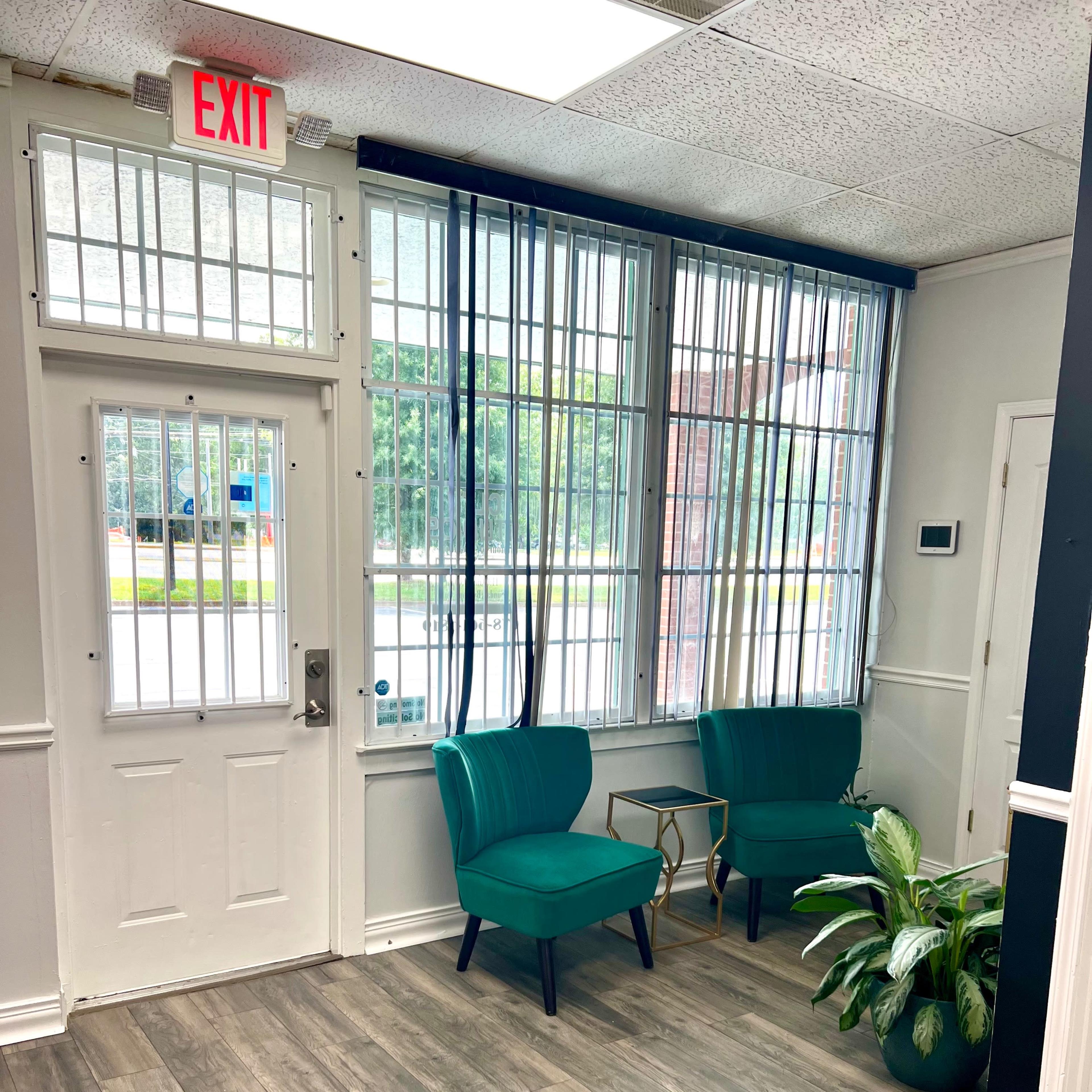 A bright entryway with two green chairs, a small table, and a large window with blinds.