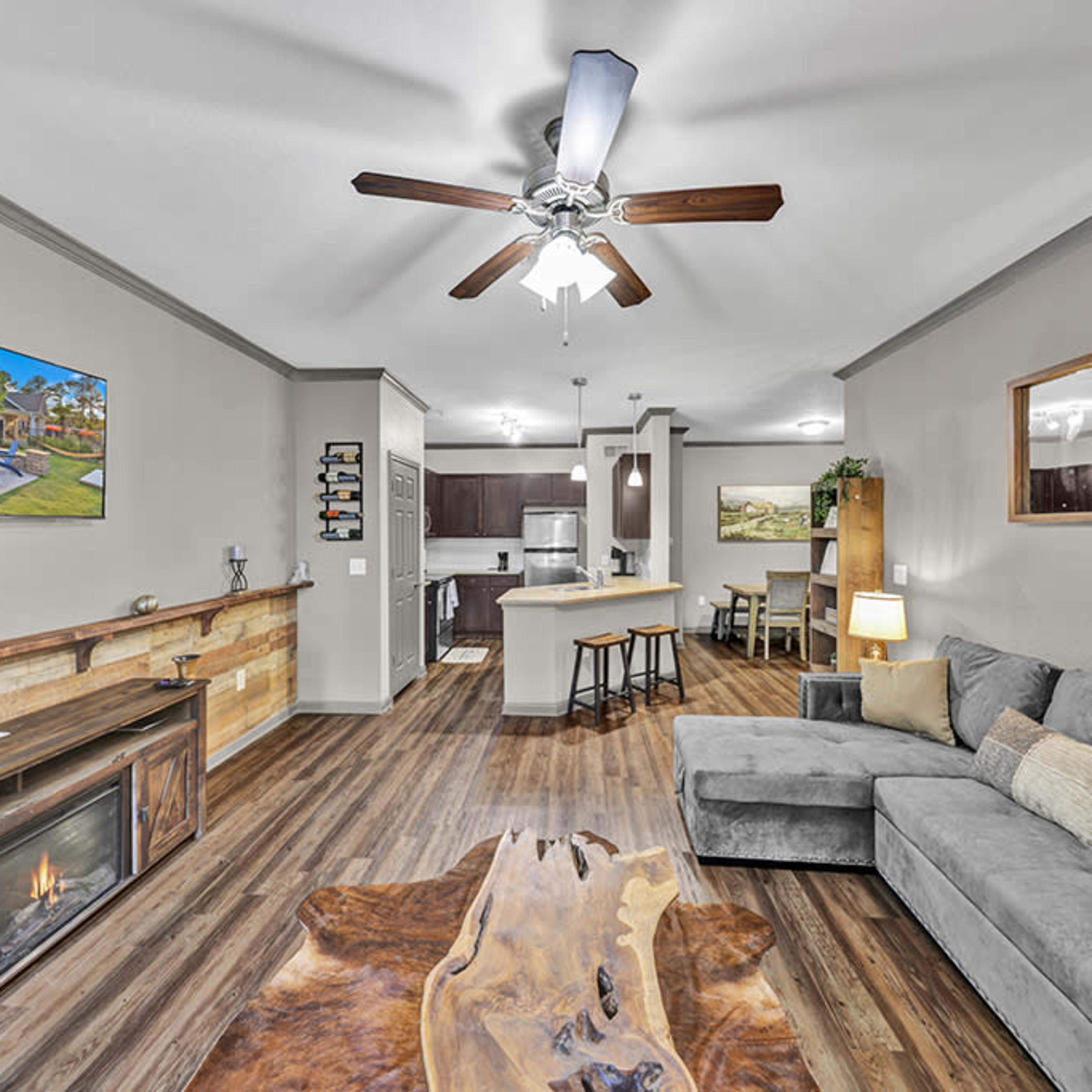 A modern living room with a gray sofa, wooden coffee table, and a television mounted on the wall, adjacent to an open kitchen area.