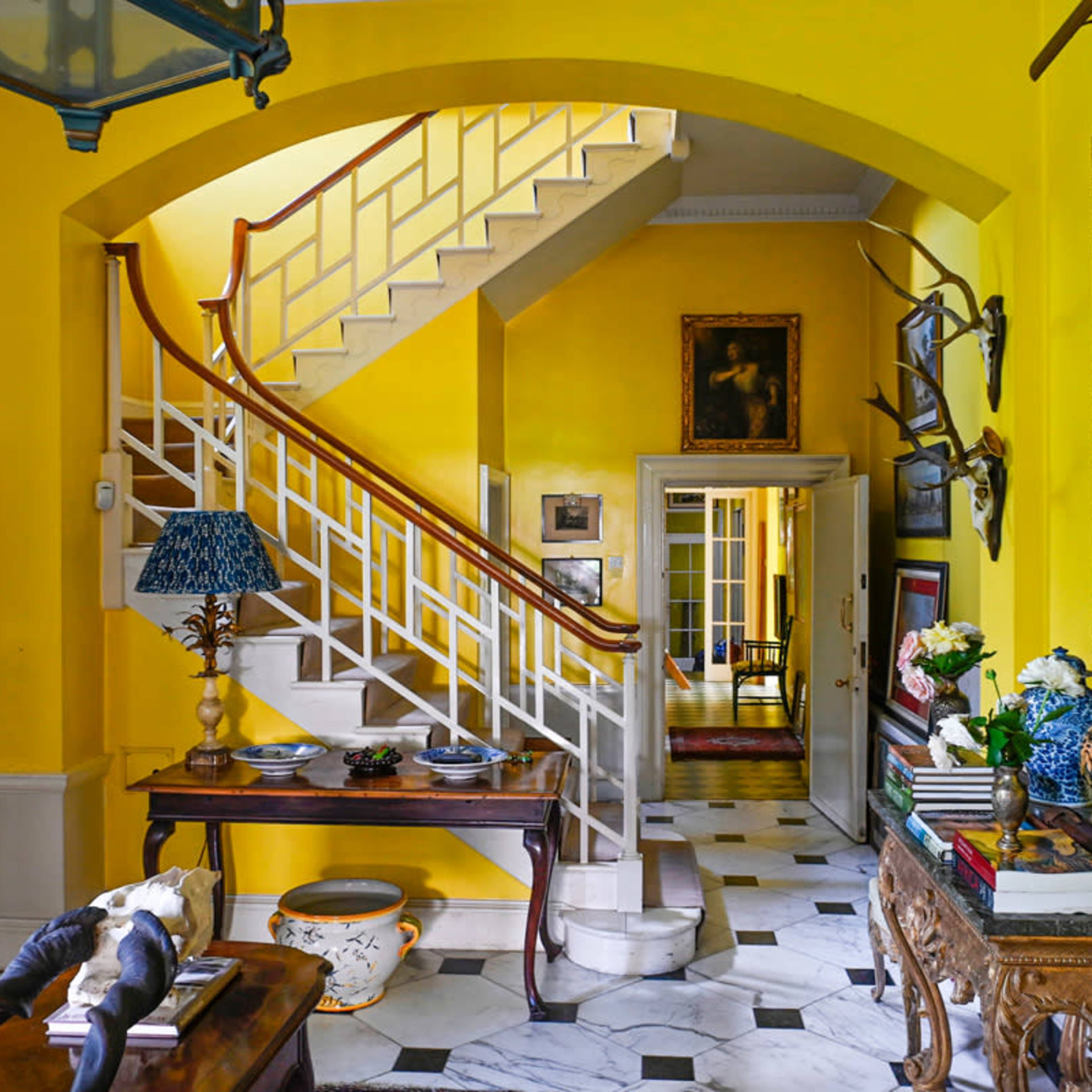 A bright yellow hallway featuring a staircase, a console table with decorative items, and artwork on the walls.