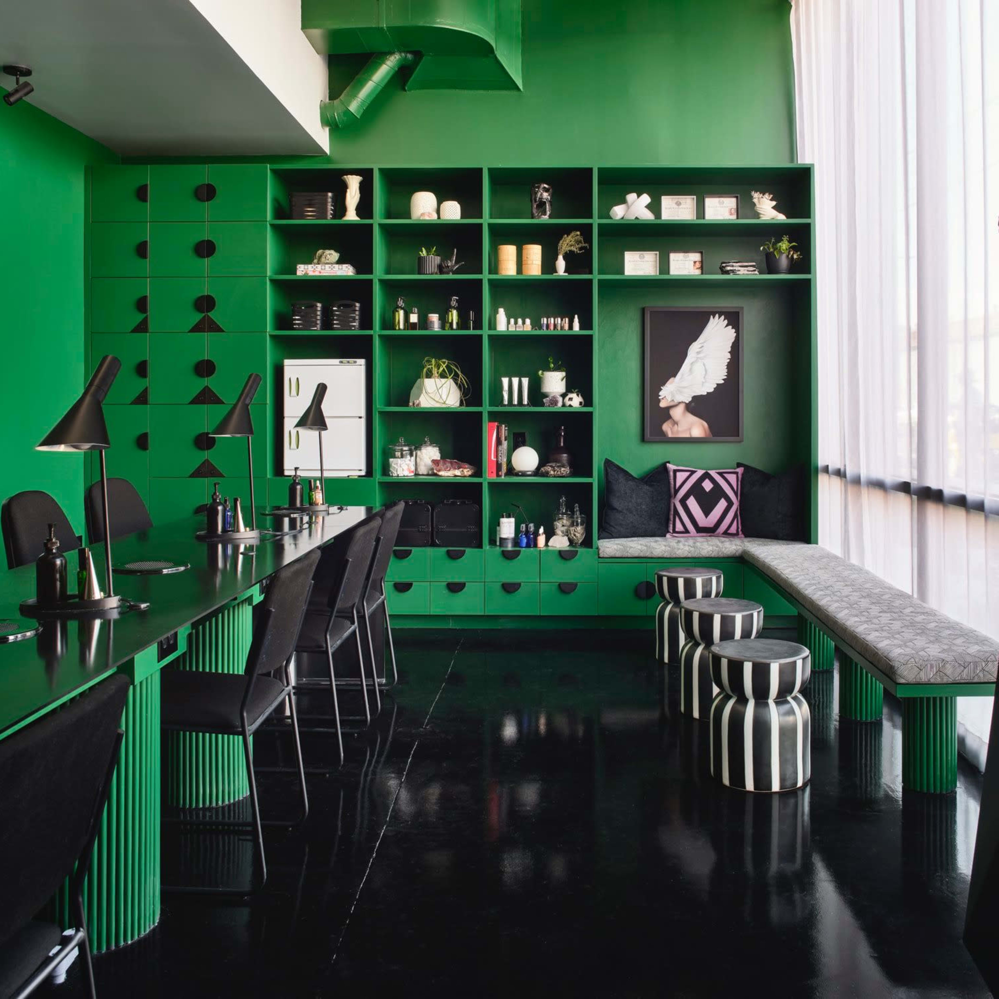 A modern interior space featuring green walls and furniture, a long table with black chairs, and a bench, all arranged with decorative shelves displaying various items.