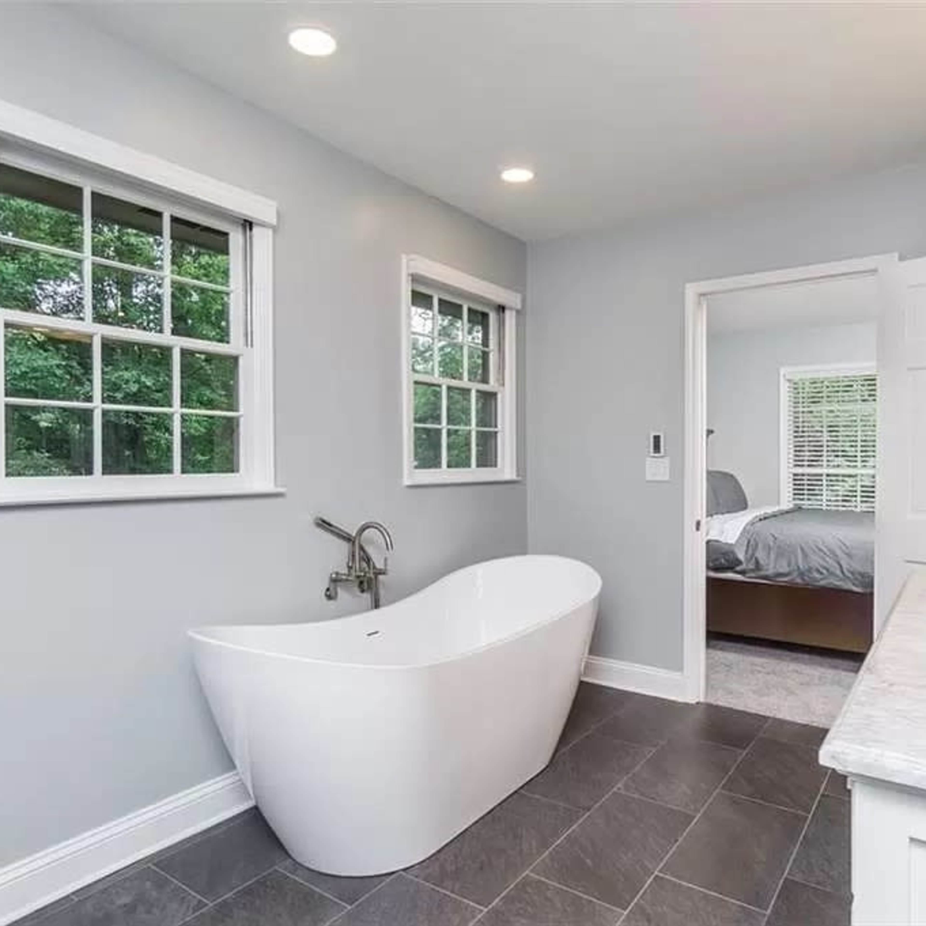 A modern bathroom featuring a freestanding bathtub, dual sinks, and windows that allow natural light to enter.