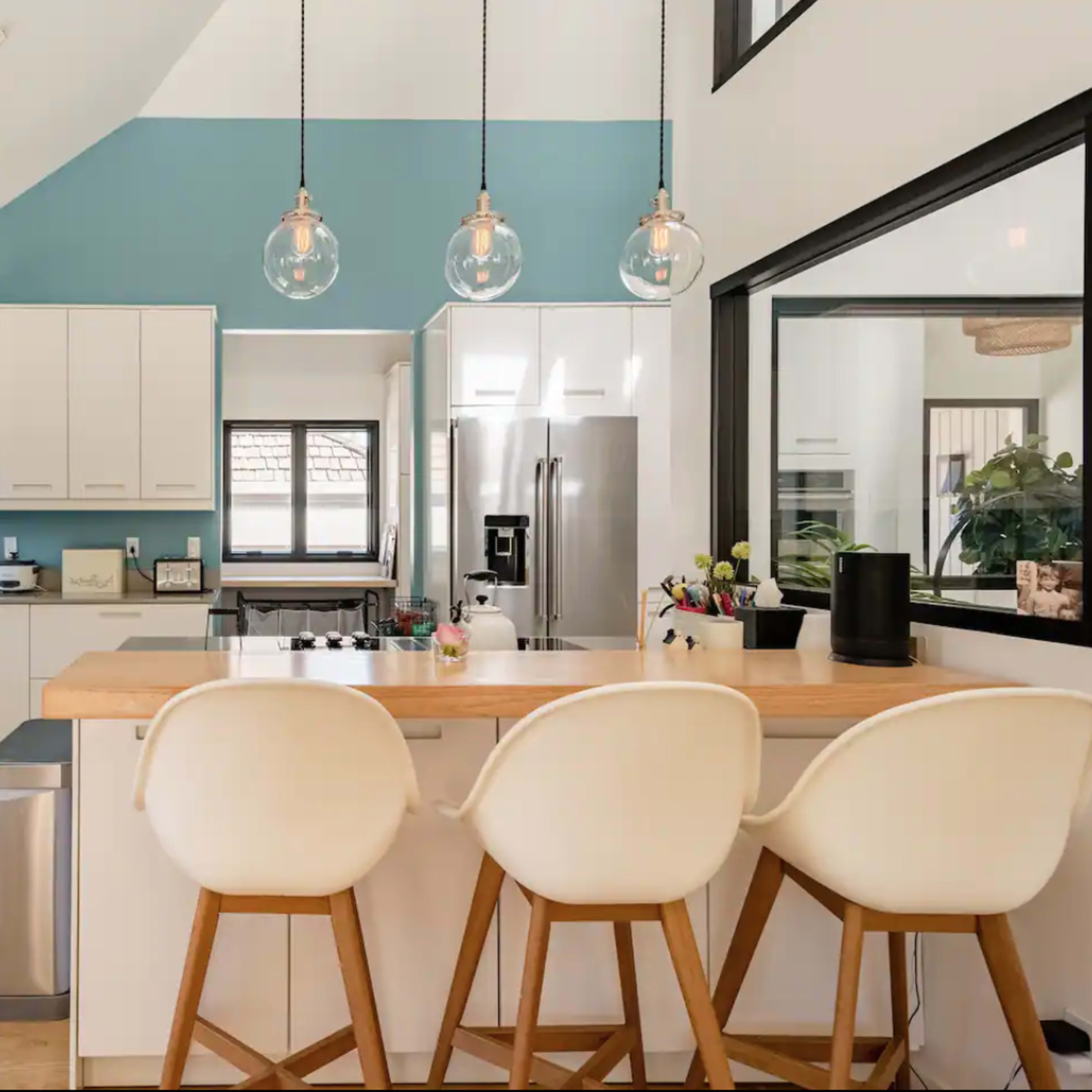 A modern kitchen features a combination of light cabinetry, a blue accent wall, and a wooden island with three bar stools.