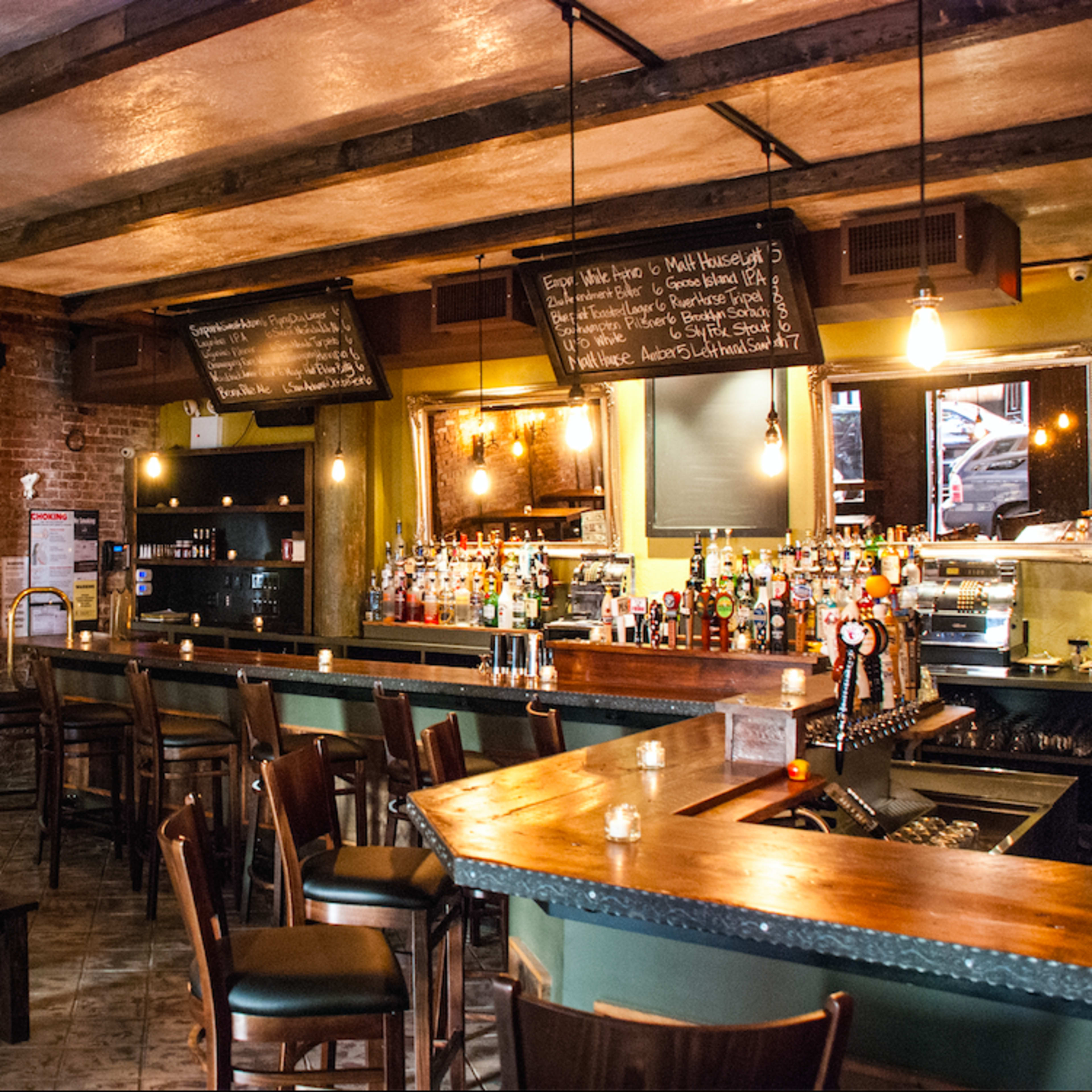 The interior of a rustic bar features exposed brick walls, wooden beams, and a well-stocked bar with various bottles and taps.