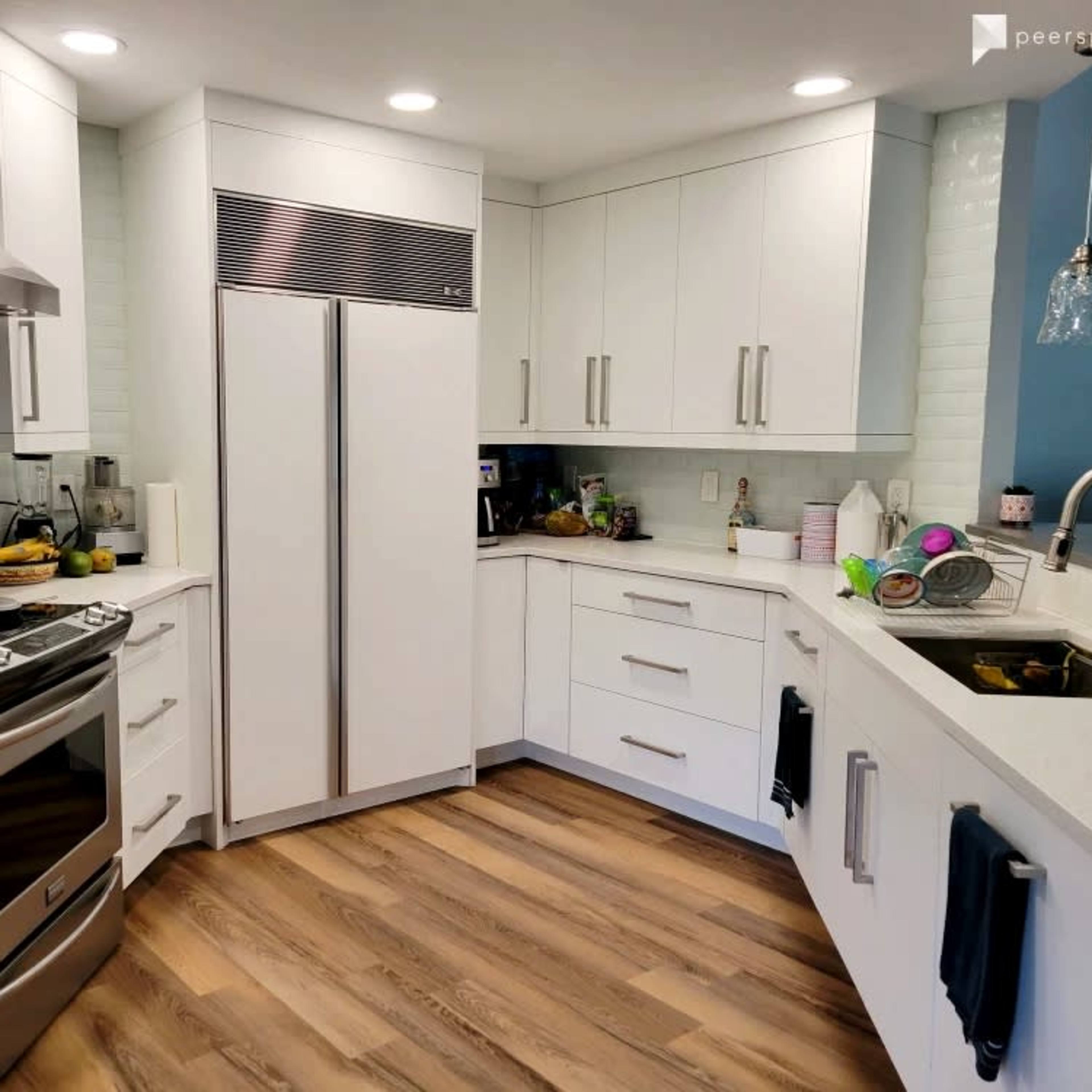 A modern kitchen with white cabinetry, stainless steel appliances, and wooden flooring.