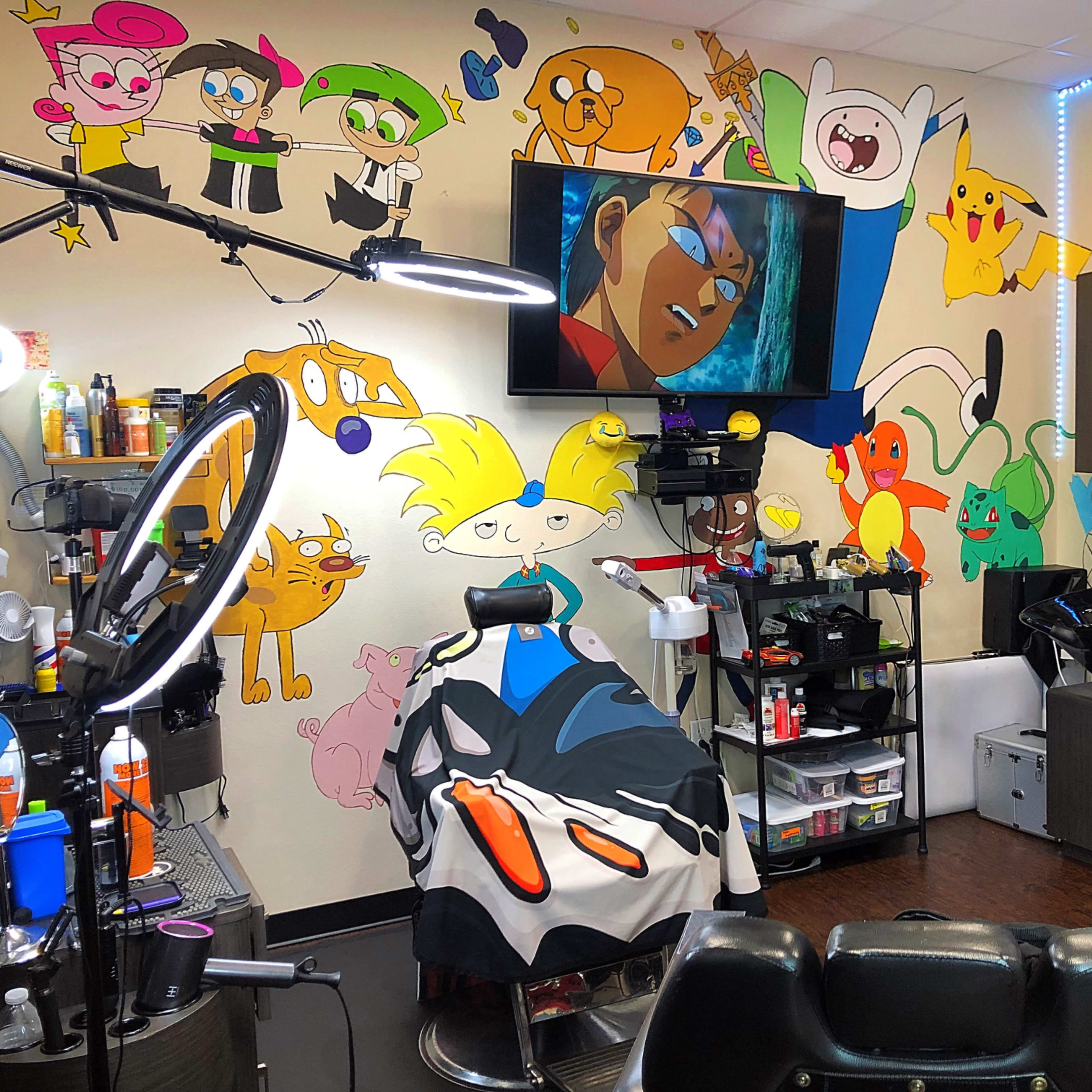 A brightly decorated barbershop with cartoon murals on the walls, a barber chair with a patterned cape, and various styling tools and products arranged on shelves.