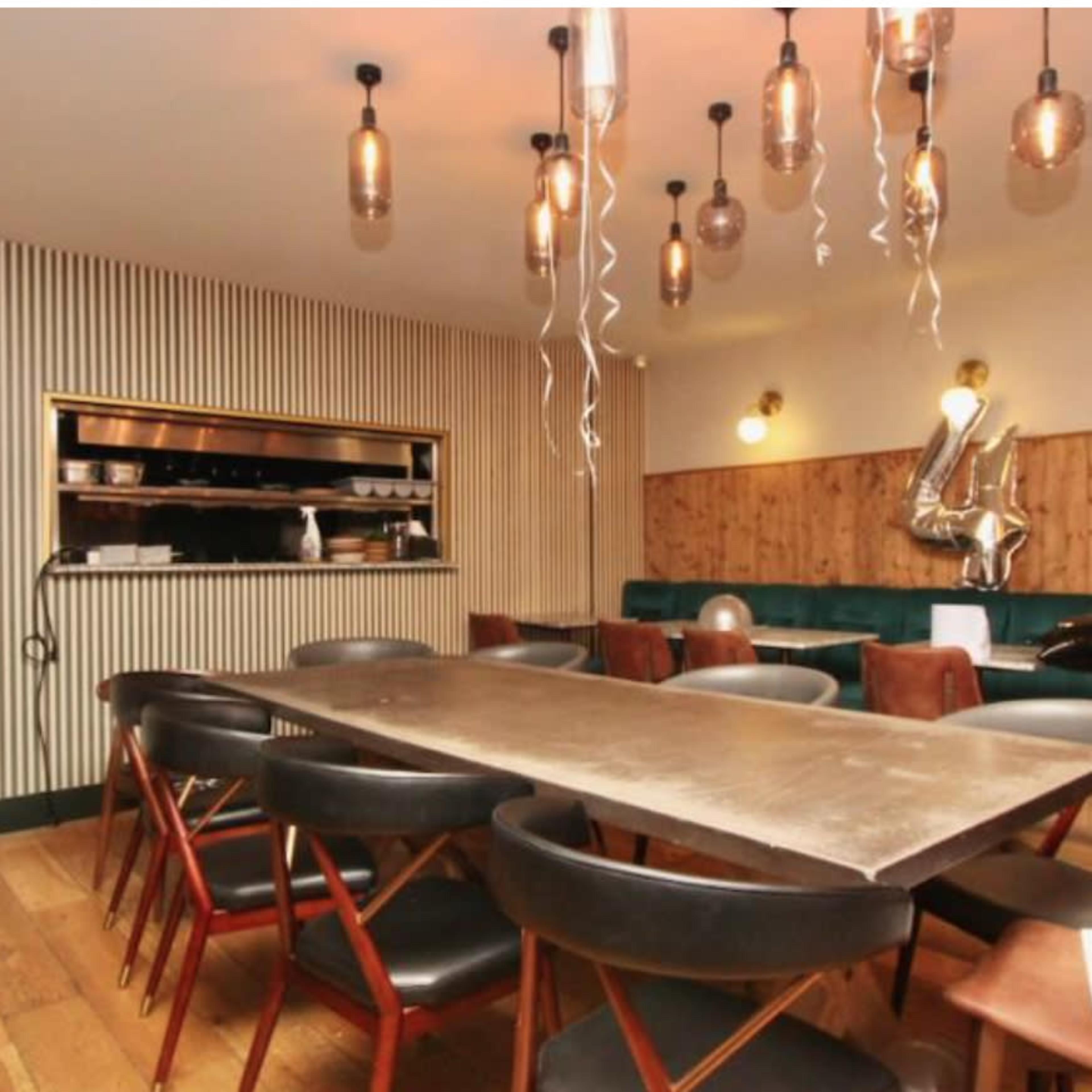 A modern dining room features a long table surrounded by black chairs, with decorative balloons spelling out "40" and hanging light fixtures overhead.