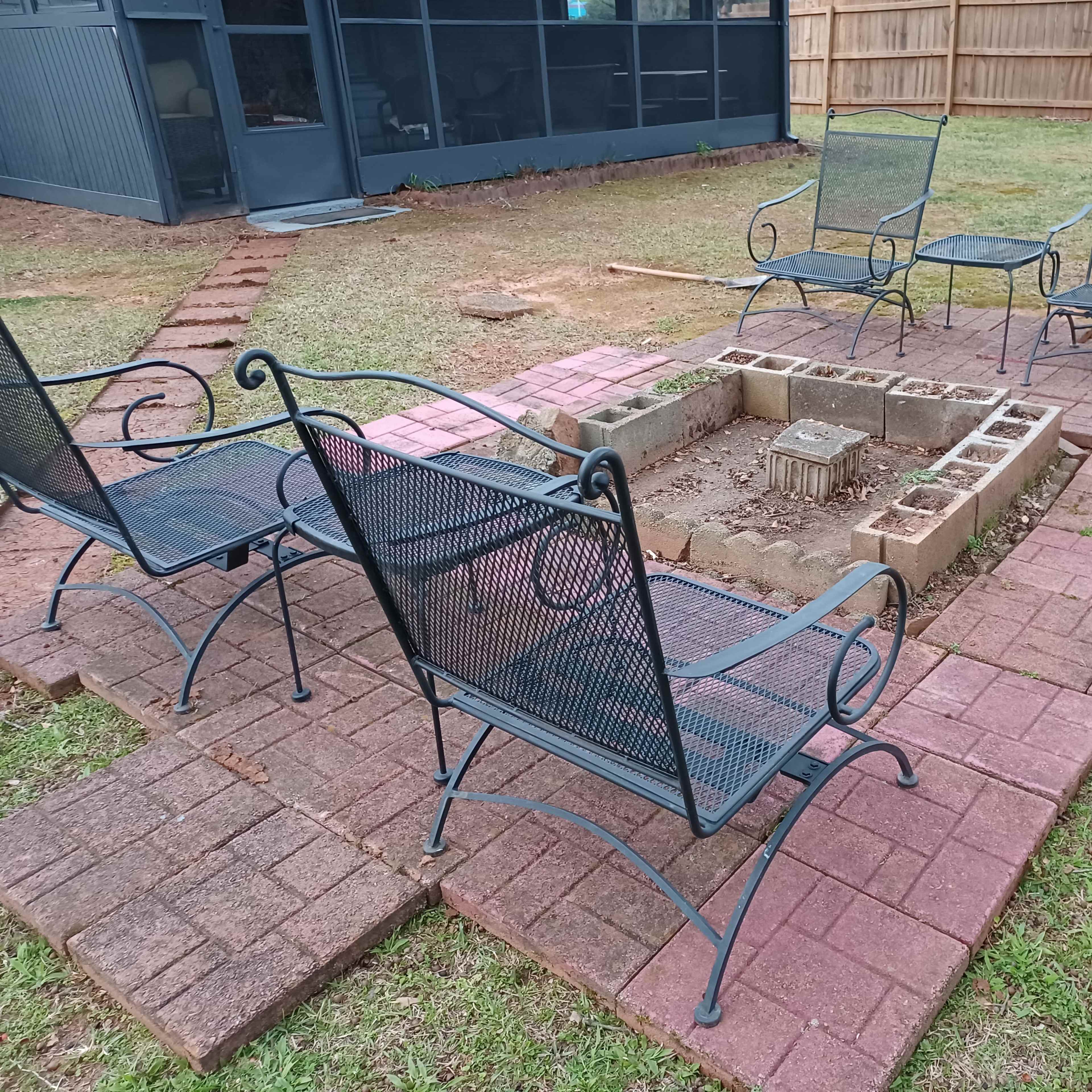 A circular fire pit area surrounded by four metal chairs, all situated on a brick patio in a grassy backyard.
