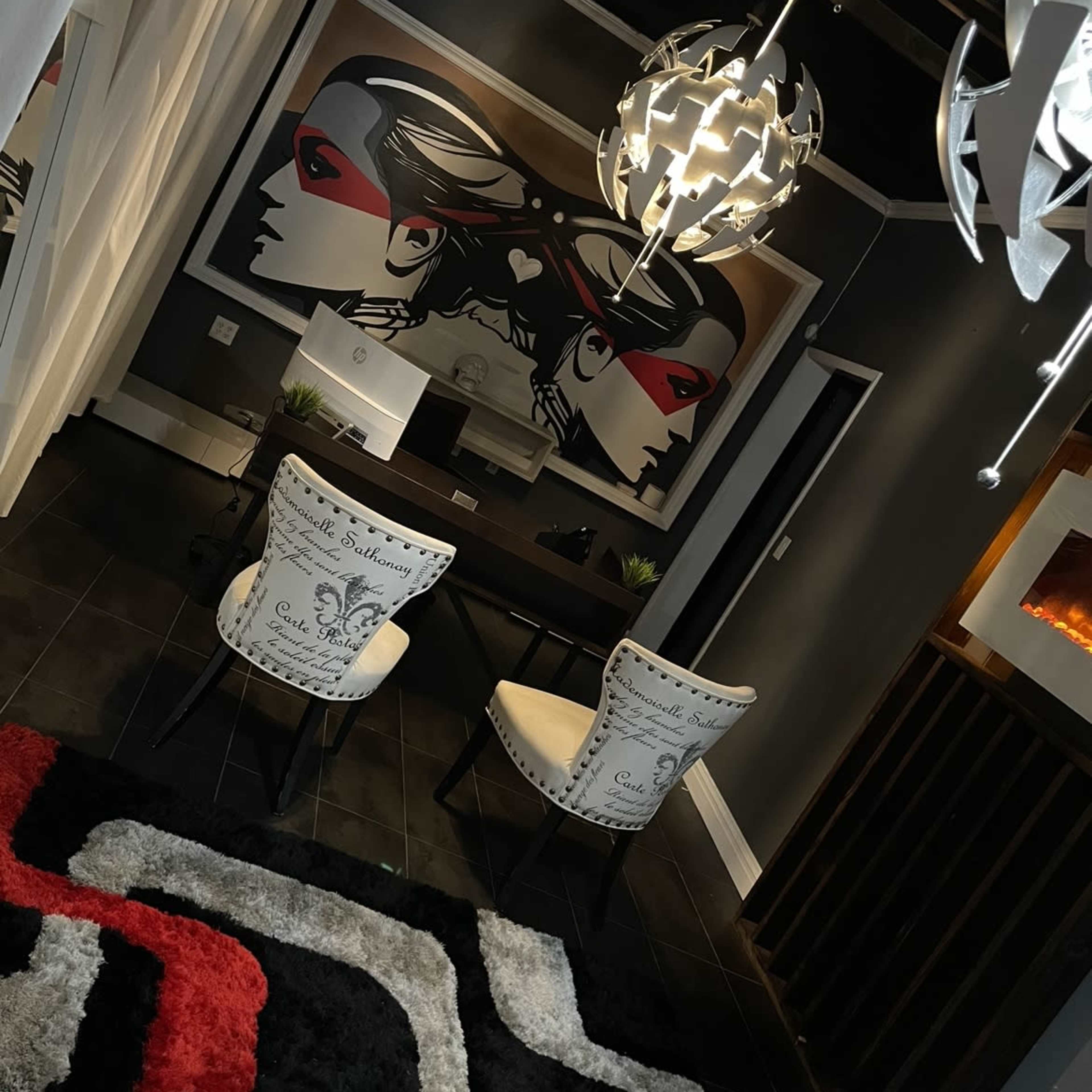 A modern interior design featuring two chairs facing a large artwork on the wall, with a decorative rug and unique light fixtures overhead.