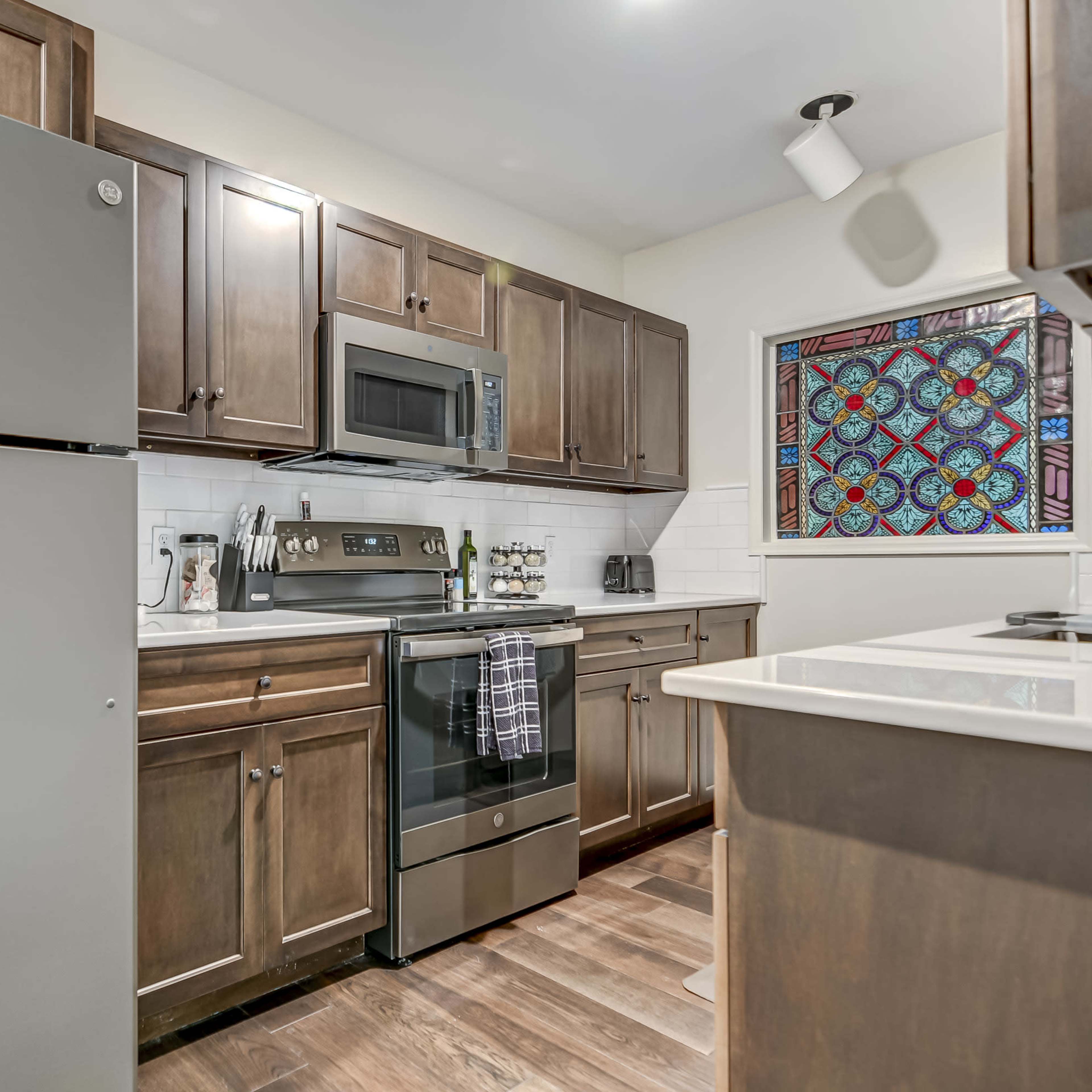 A modern kitchen features stainless steel appliances, dark wood cabinets, and a colorful stained glass window.
