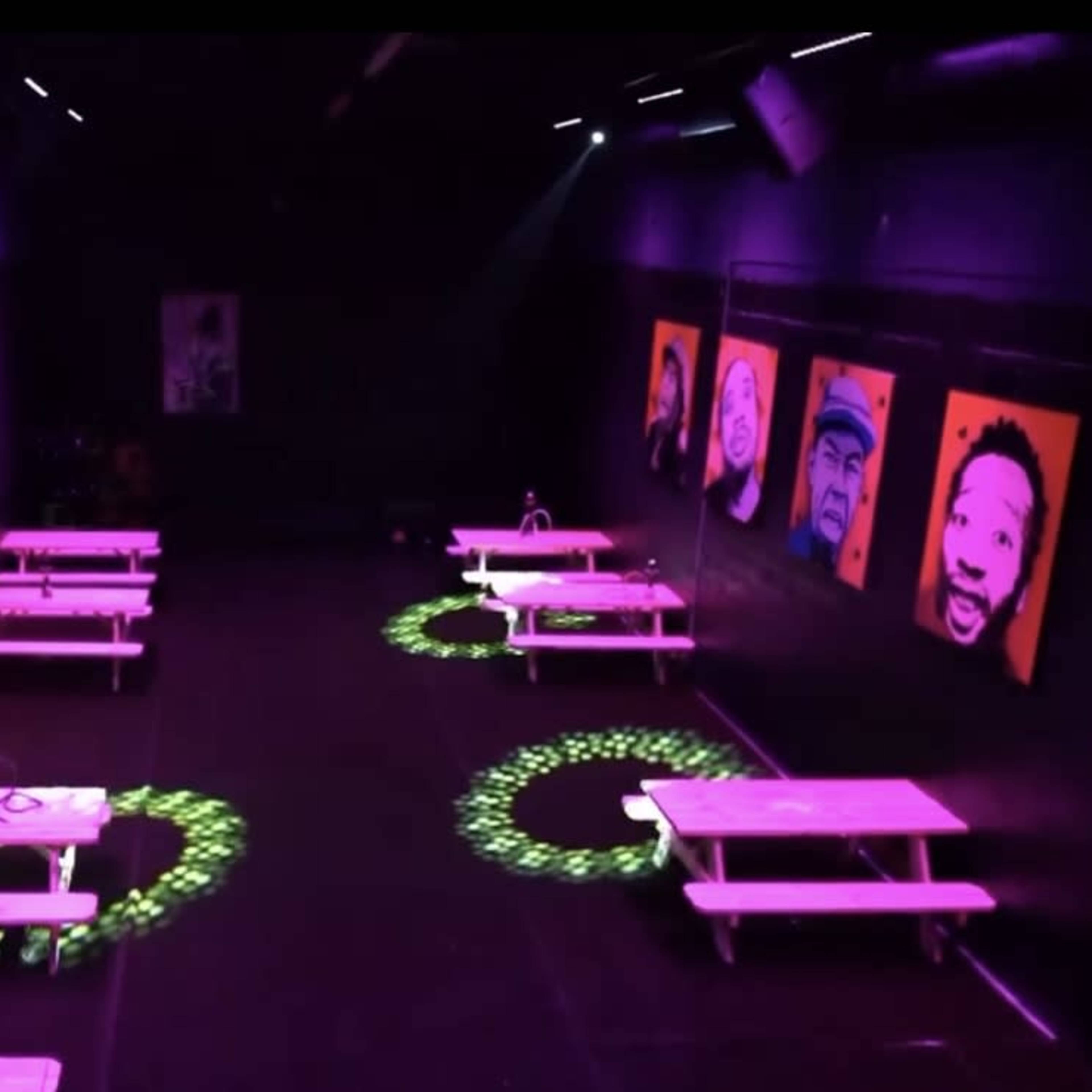 A dimly lit room with purple lighting, several tables arranged in rows, and colorful portraits hanging on the walls.