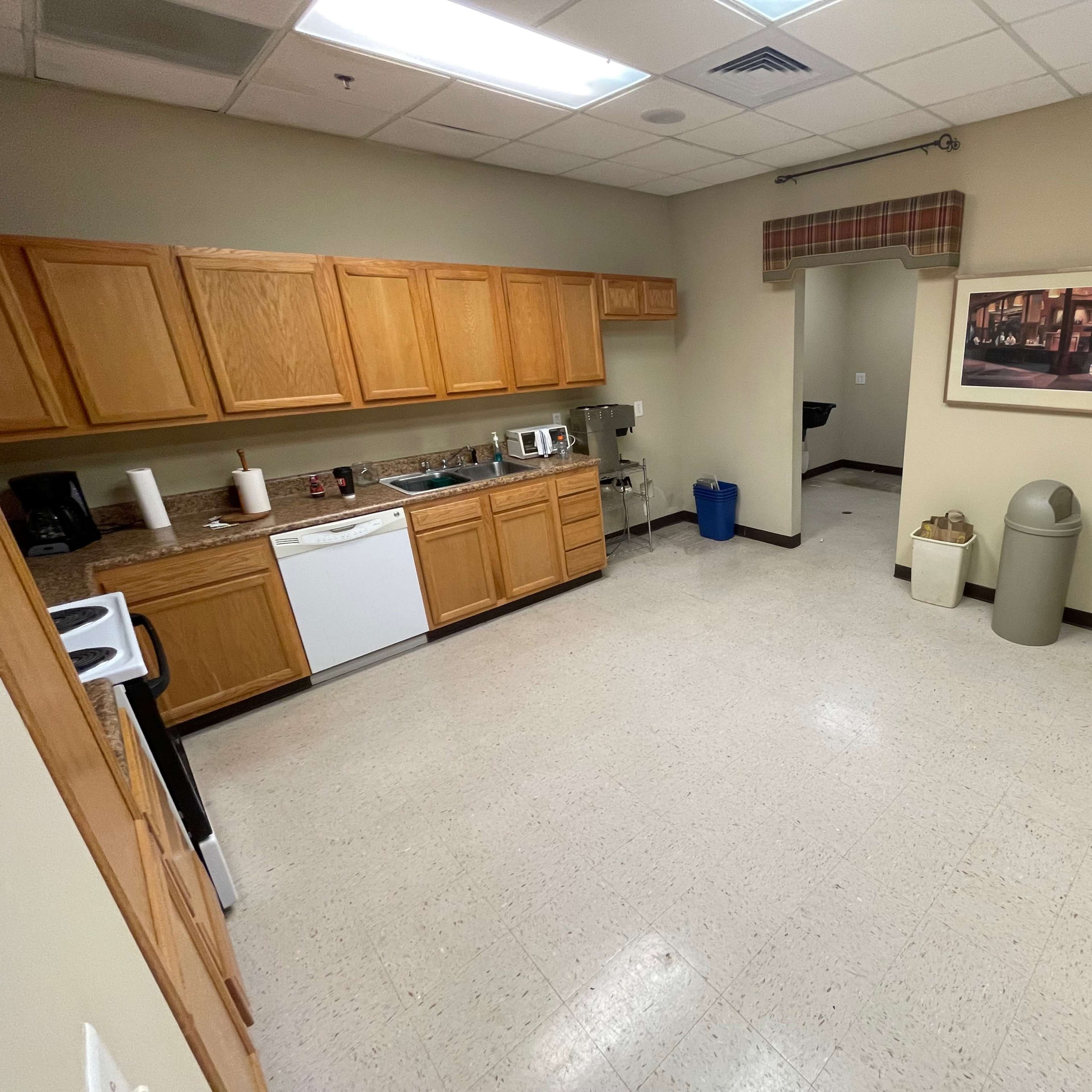 A clean kitchen area with wooden cabinets, a counter with appliances, and a door leading to a restroom.