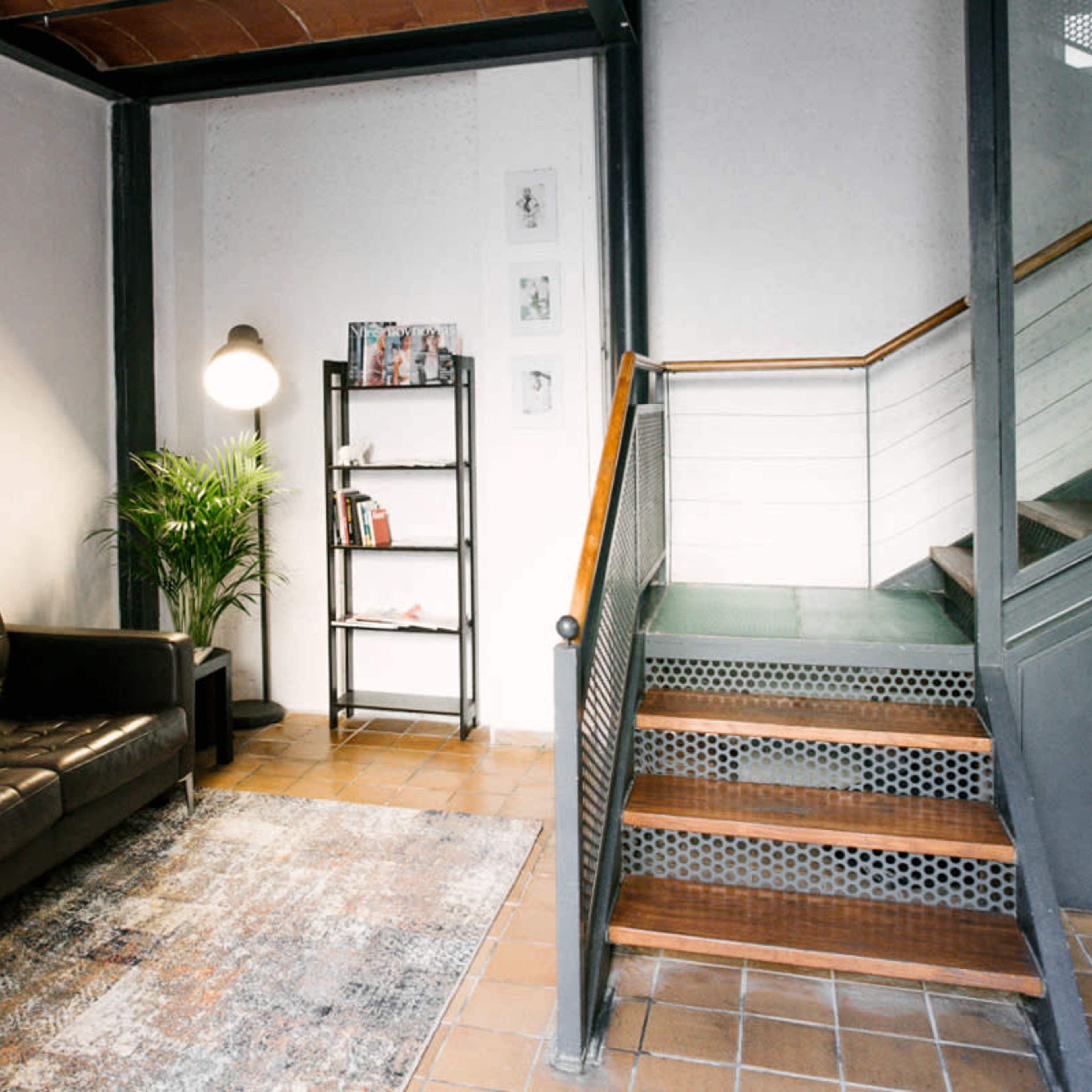 A modern entryway with a black leather sofa, a book shelf, a potted plant, and a staircase leading to an upper level.