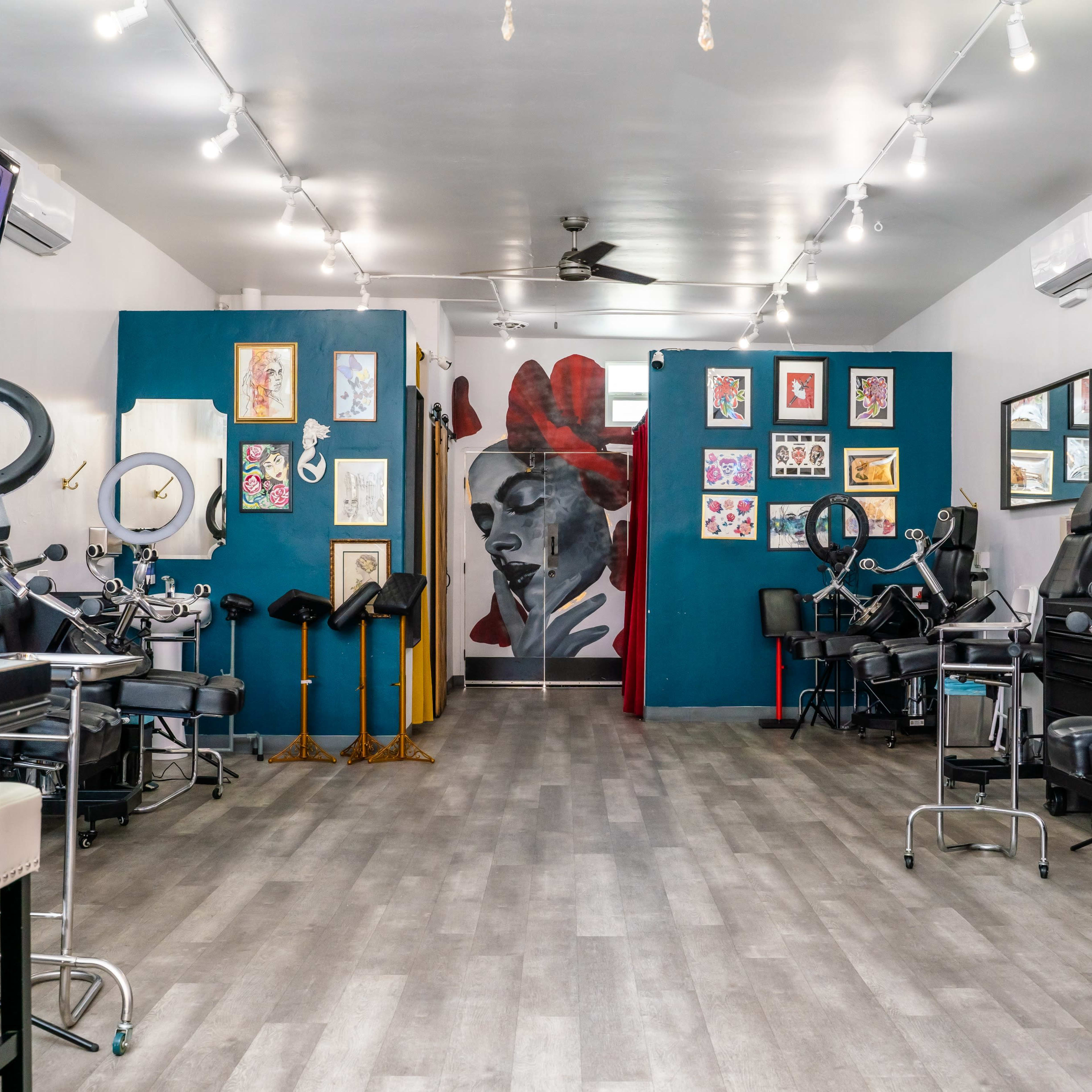 The interior of a tattoo studio featuring multiple tattoo stations, artwork on the walls, and a large mural at the back.