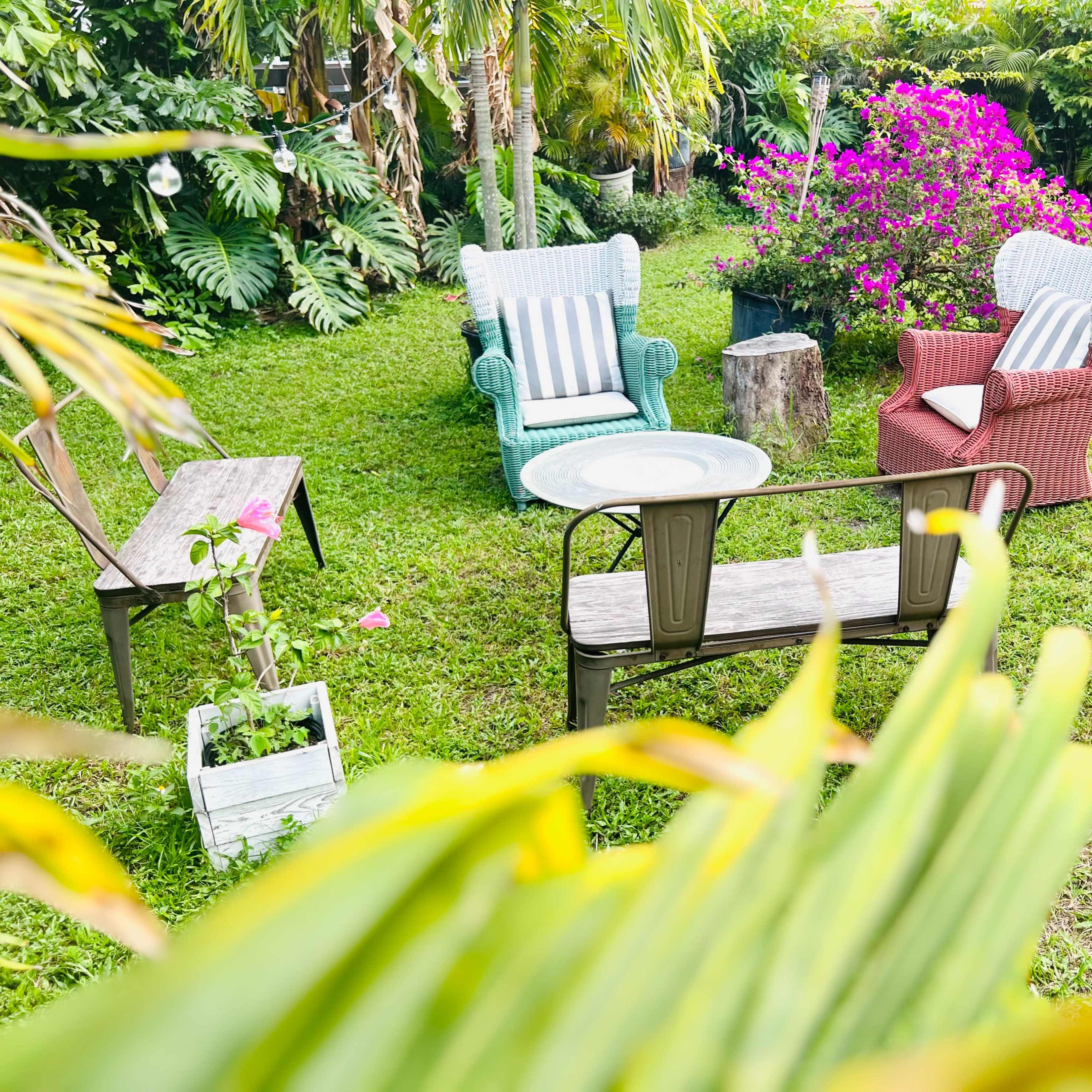 A garden with a green lawn, colorful armchairs, a wooden bench, a small table, and blooming purple flowers.