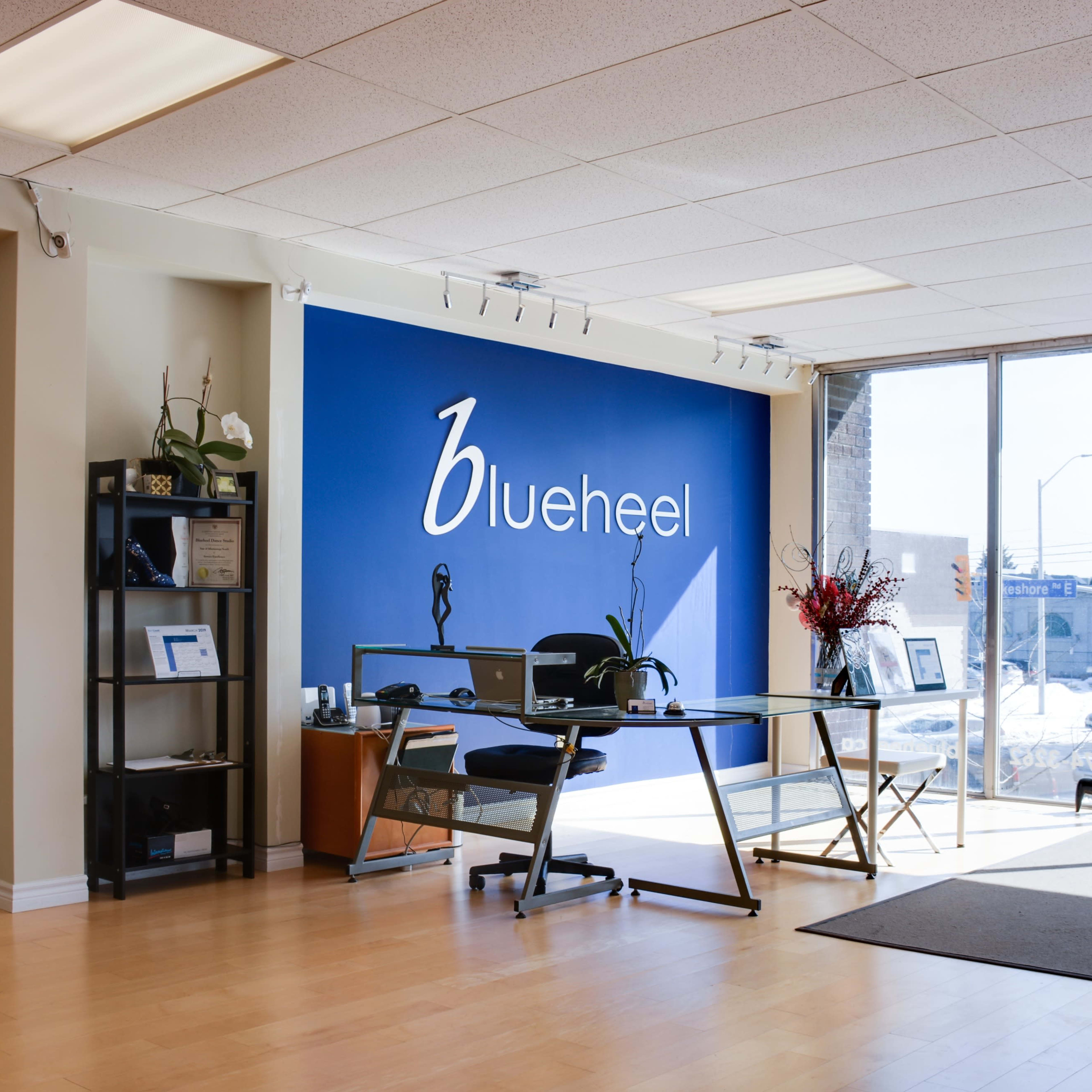 A modern office space with a blue accent wall featuring the logo "blueheel," a glass desk, and a view of the city through large windows.