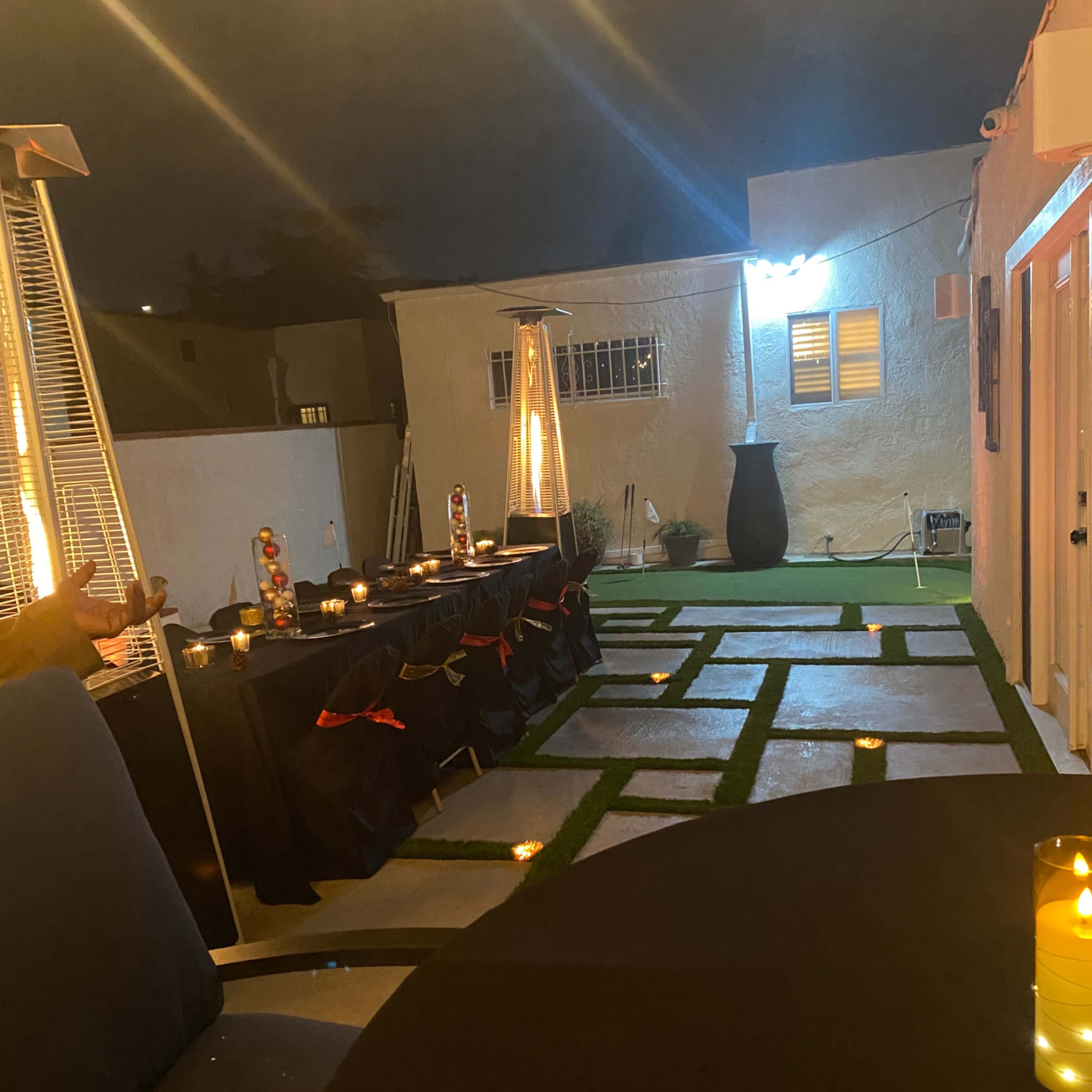 An outdoor party setup with black tablecloths, candles, and a landscaped area featuring stone pathways and patio lighting.