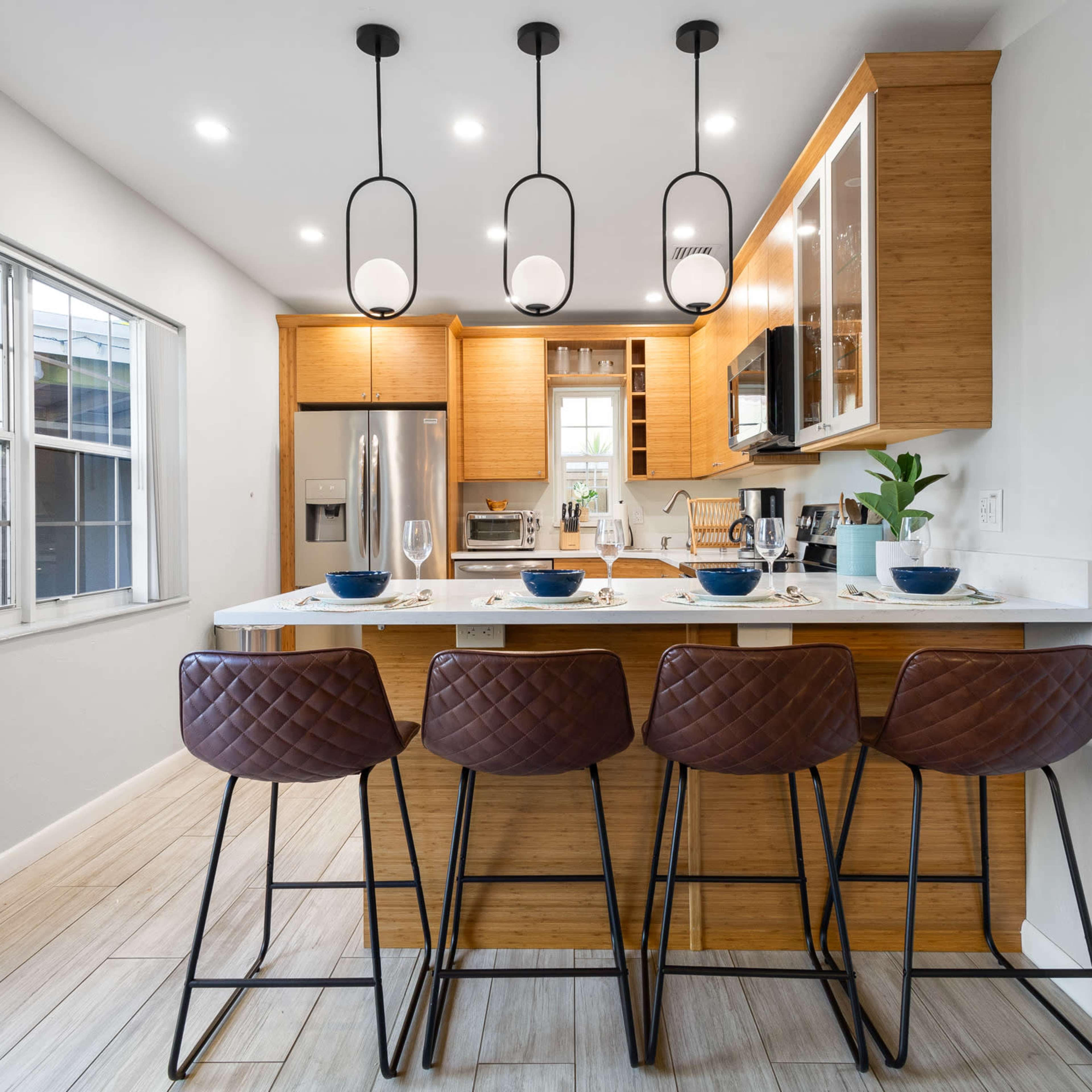 A modern kitchen features wooden cabinets, a central island with bar seating, and pendant lights above.