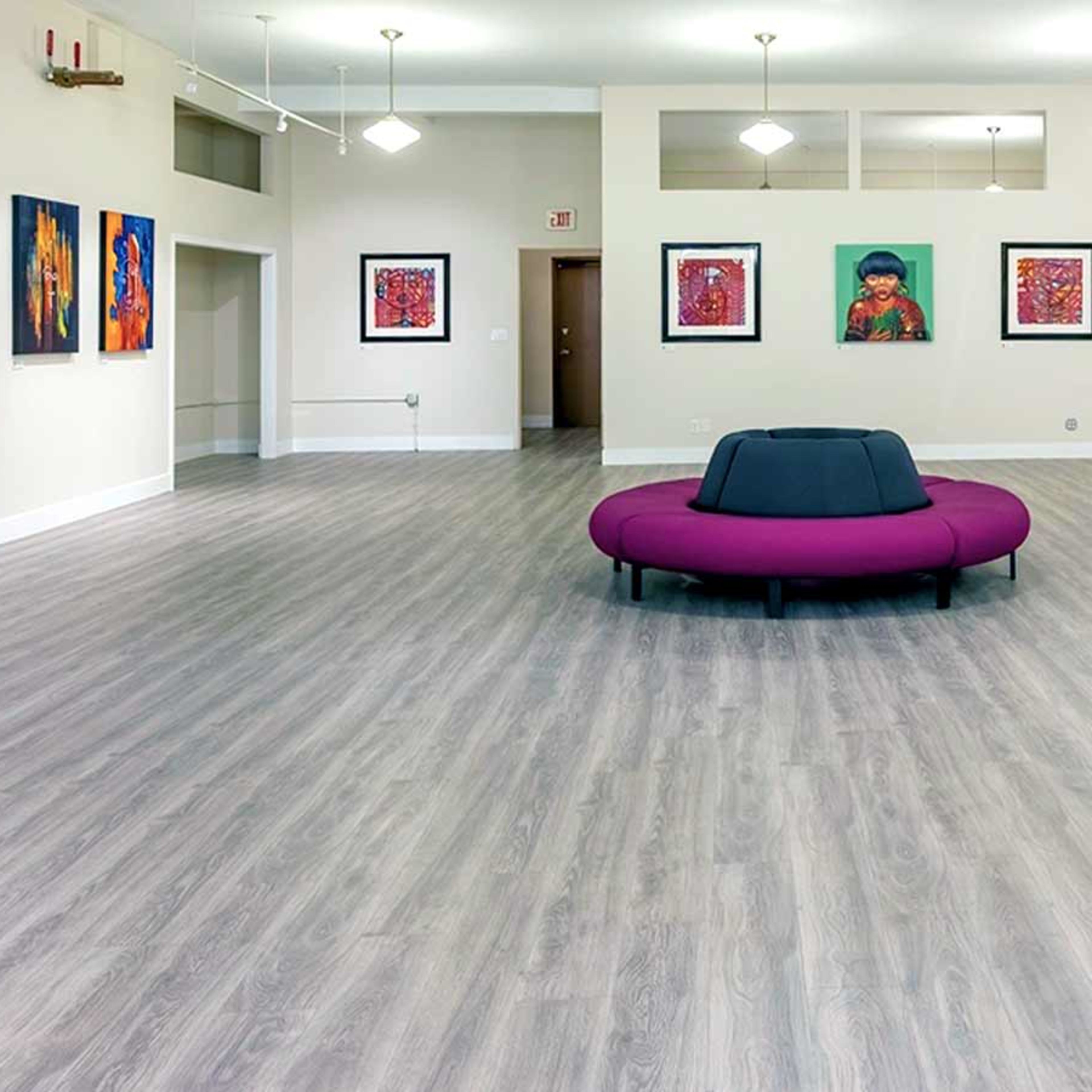 A brightly lit gallery space with a large purple seating area in the center and colorful artworks displayed on the walls.