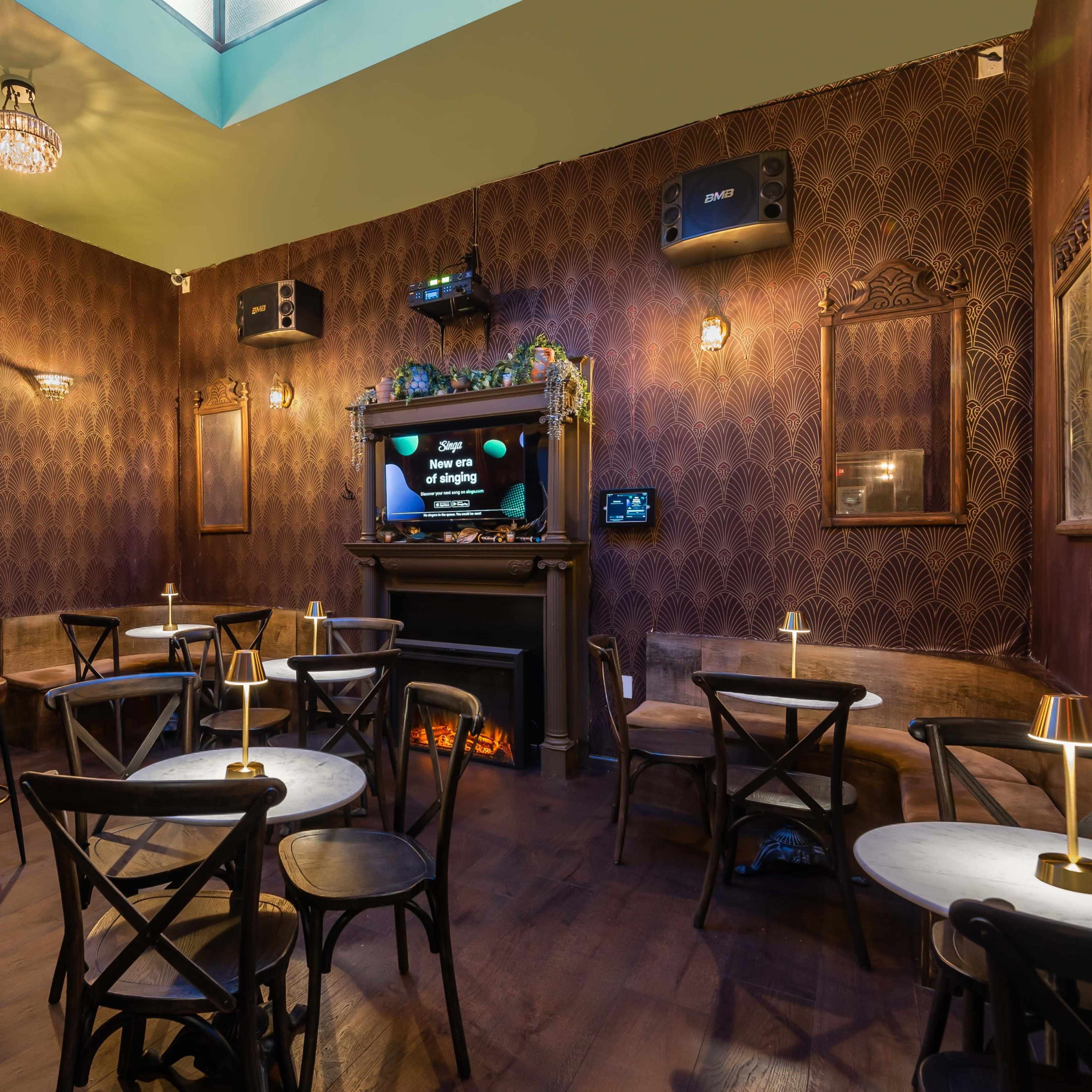 A cozy bar interior with wooden tables, a small bar area, and a wall-mounted TV, surrounded by vintage decor and warm lighting.