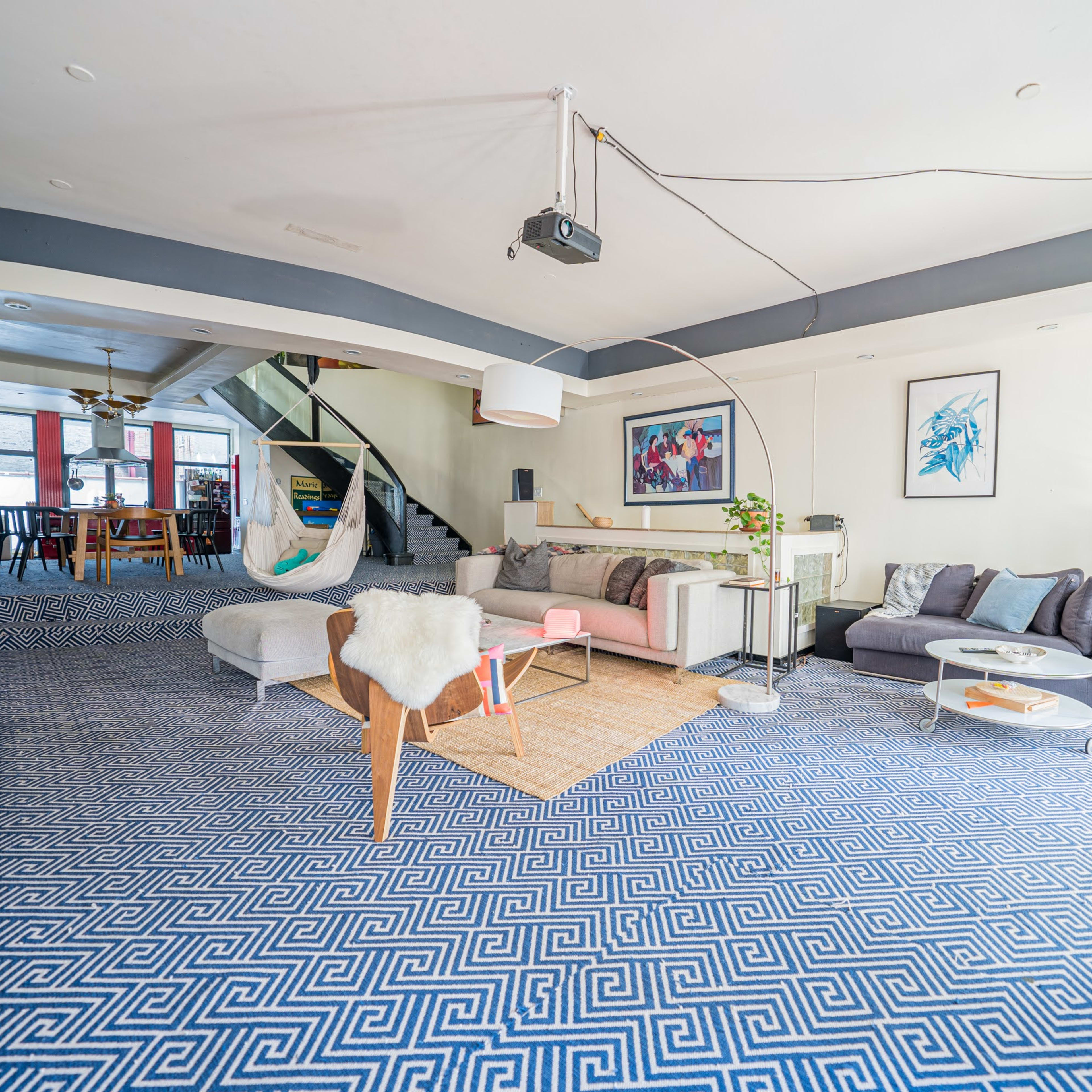 A spacious room with a patterned blue carpet, modern furniture, and an open layout that includes a staircase and various seating areas.