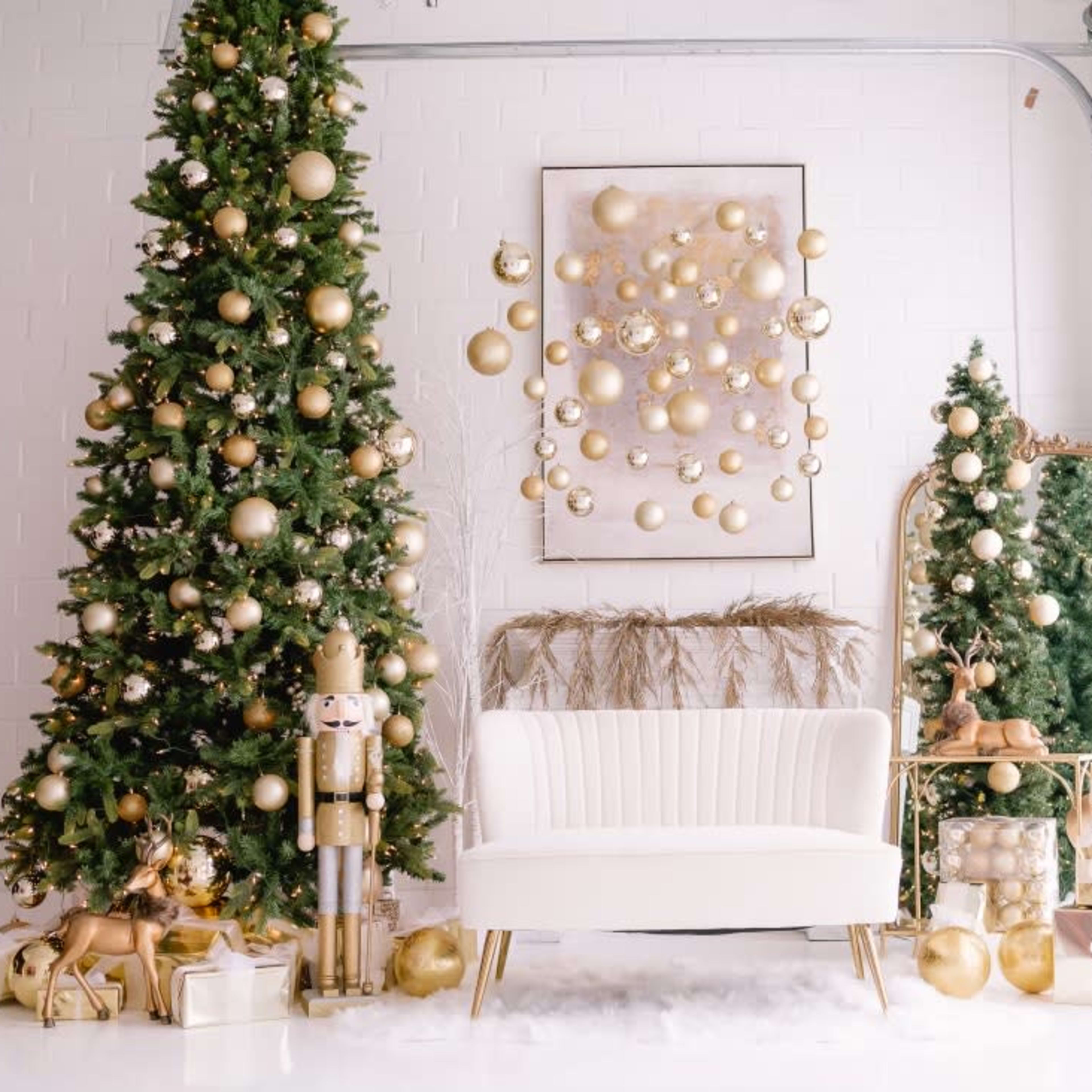 A festive indoor scene with two decorated Christmas trees, a white couch, and various gold-themed ornaments and decorations.