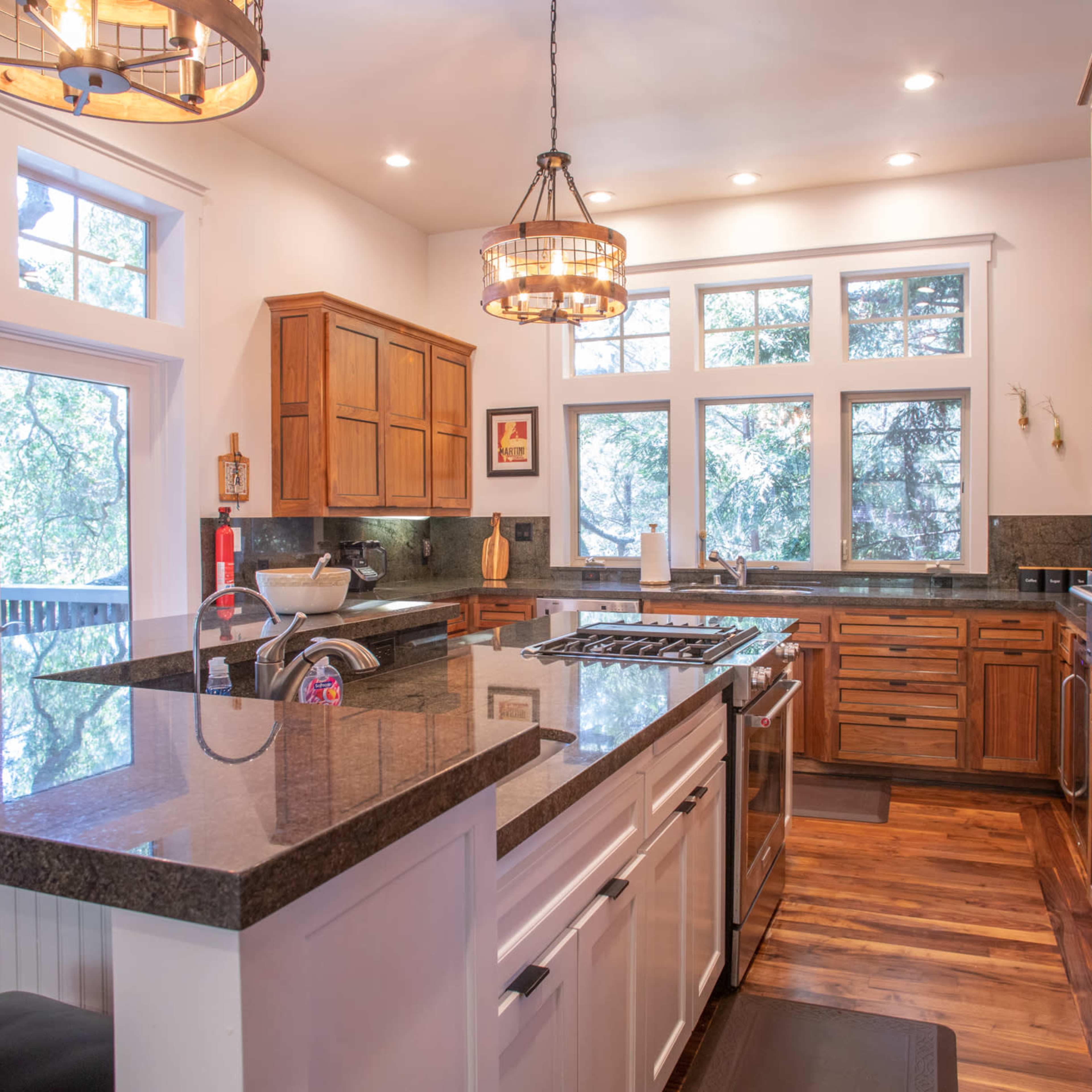 The kitchen features wooden cabinetry, a large island with a dark countertop, and multiple windows providing natural light.