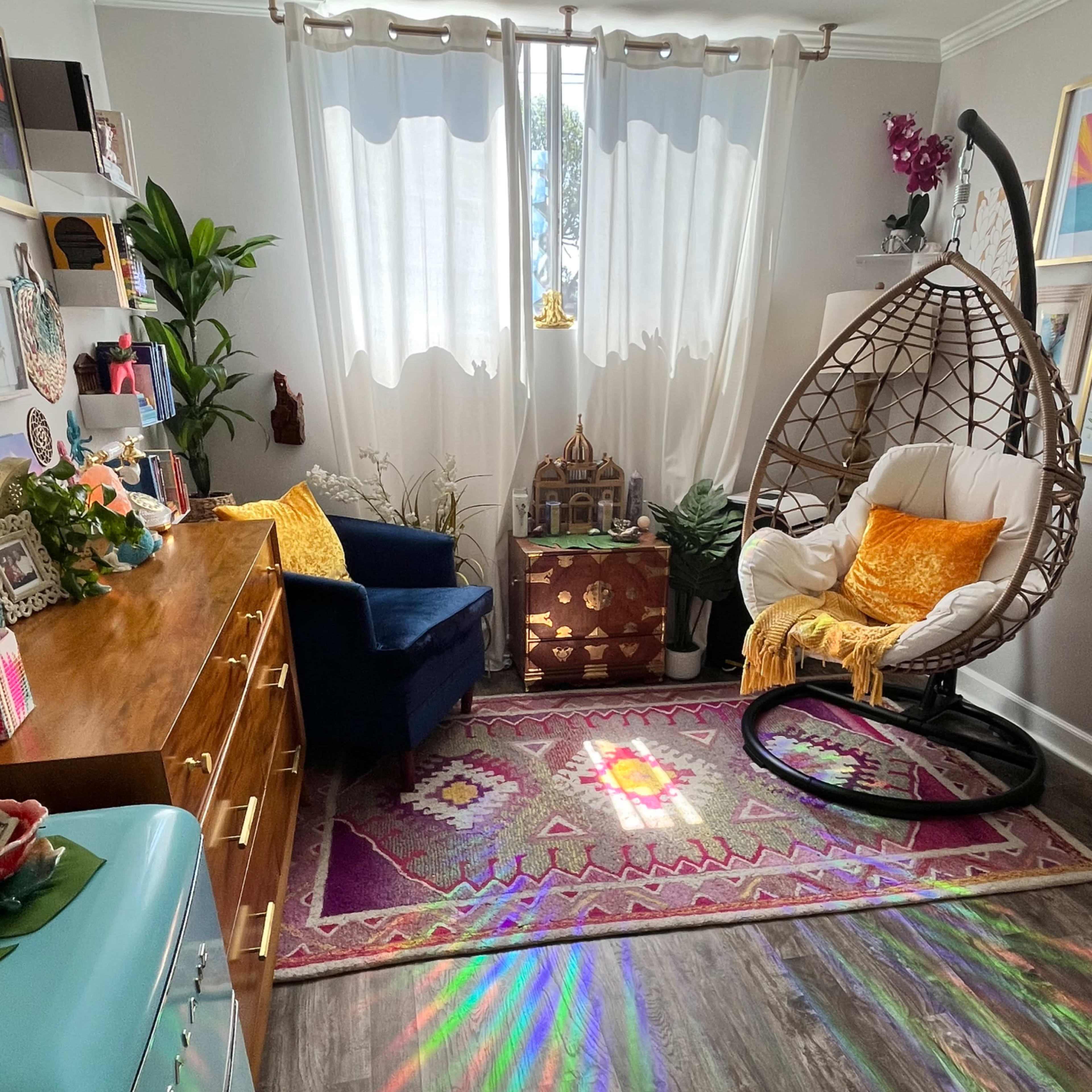A cozy room features a hanging chair, a wooden dresser, and a colorful rug with sunlight casting rainbow patterns on the floor.