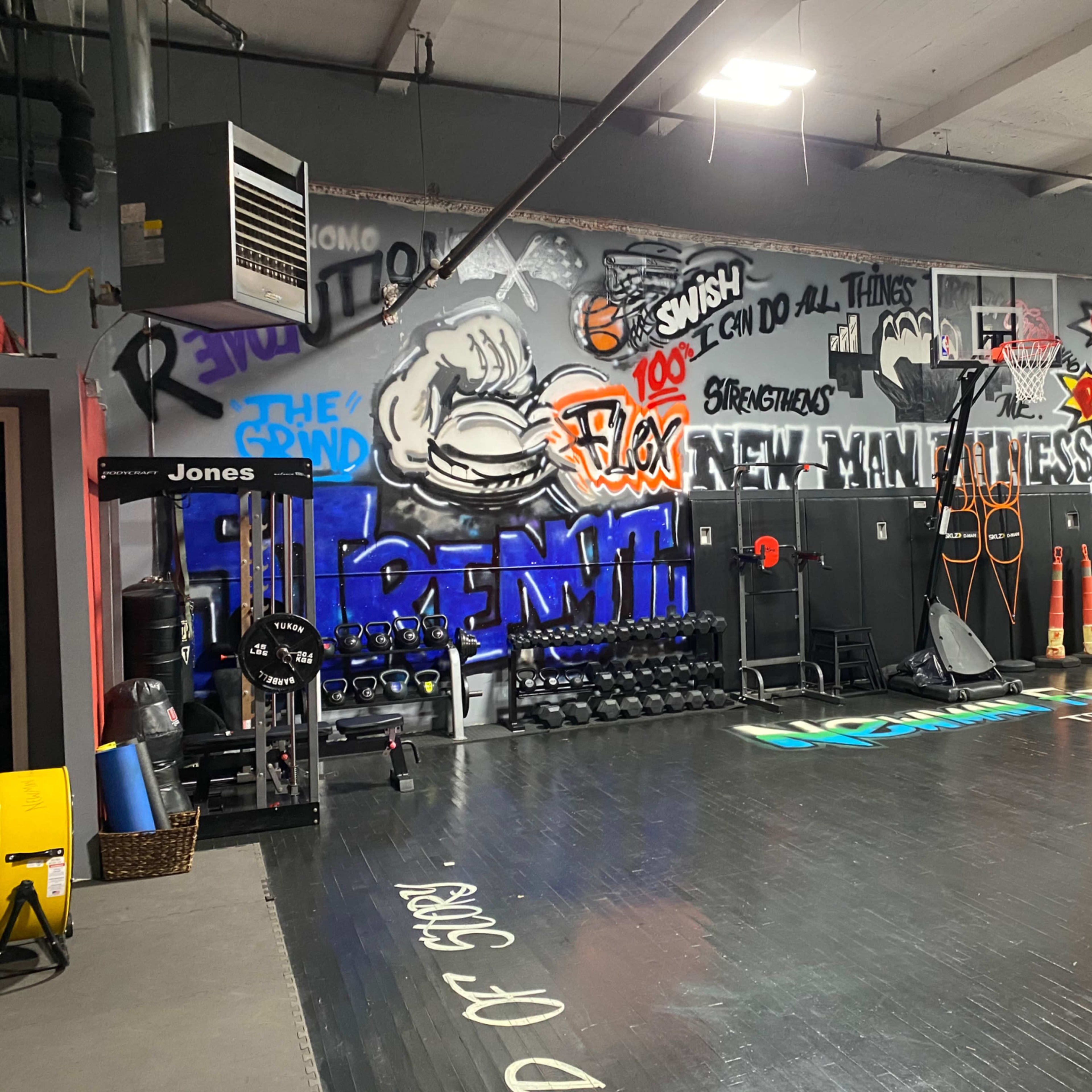 A gym interior with a variety of weights, exercise equipment, and motivational graffiti murals on the walls.
