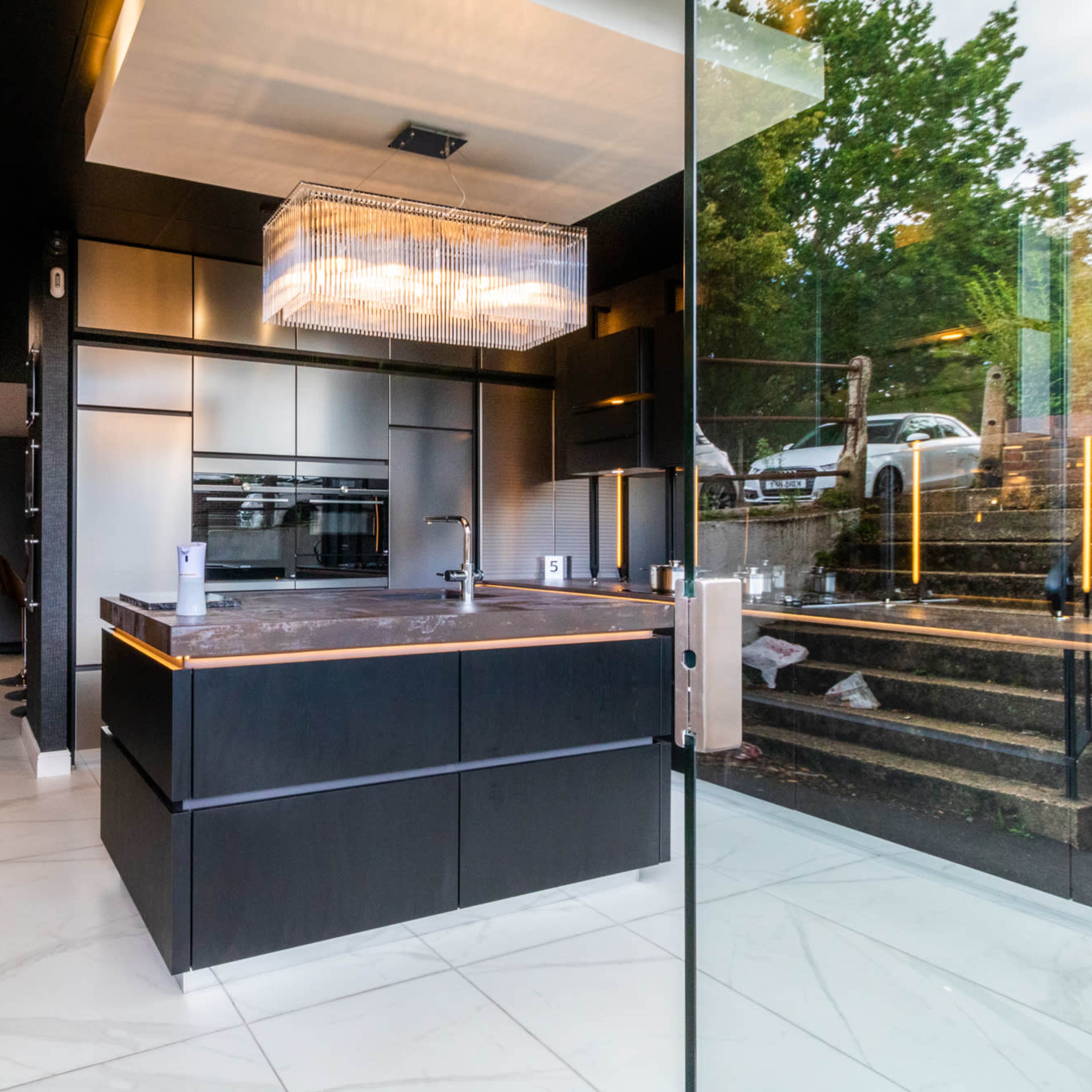A modern kitchen with sleek black cabinetry, a large island with a marble countertop, and ample natural light from glass walls.