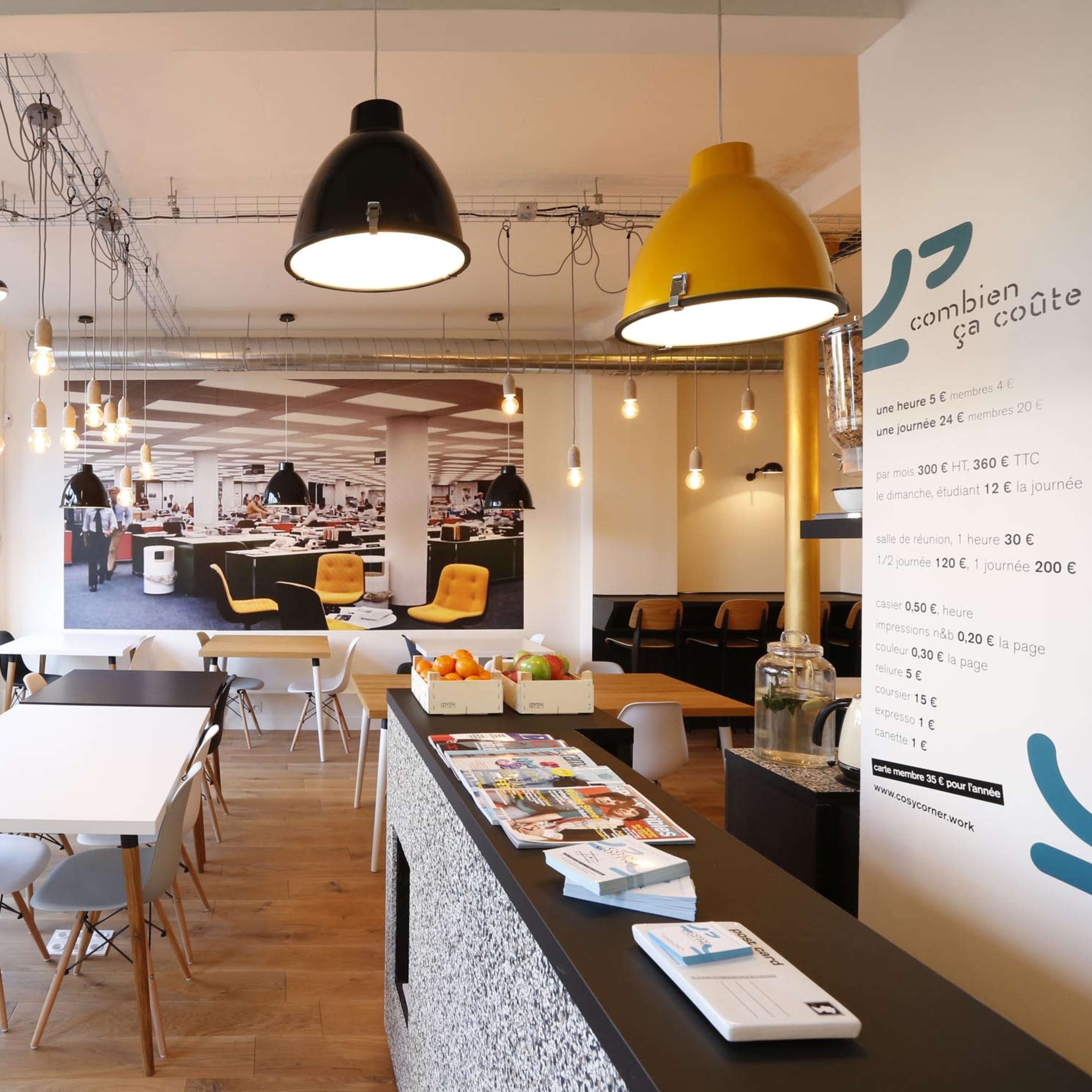 A modern café interior features a spacious seating area with a minimalist design, pendant lights, and a counter displaying informational brochures.
