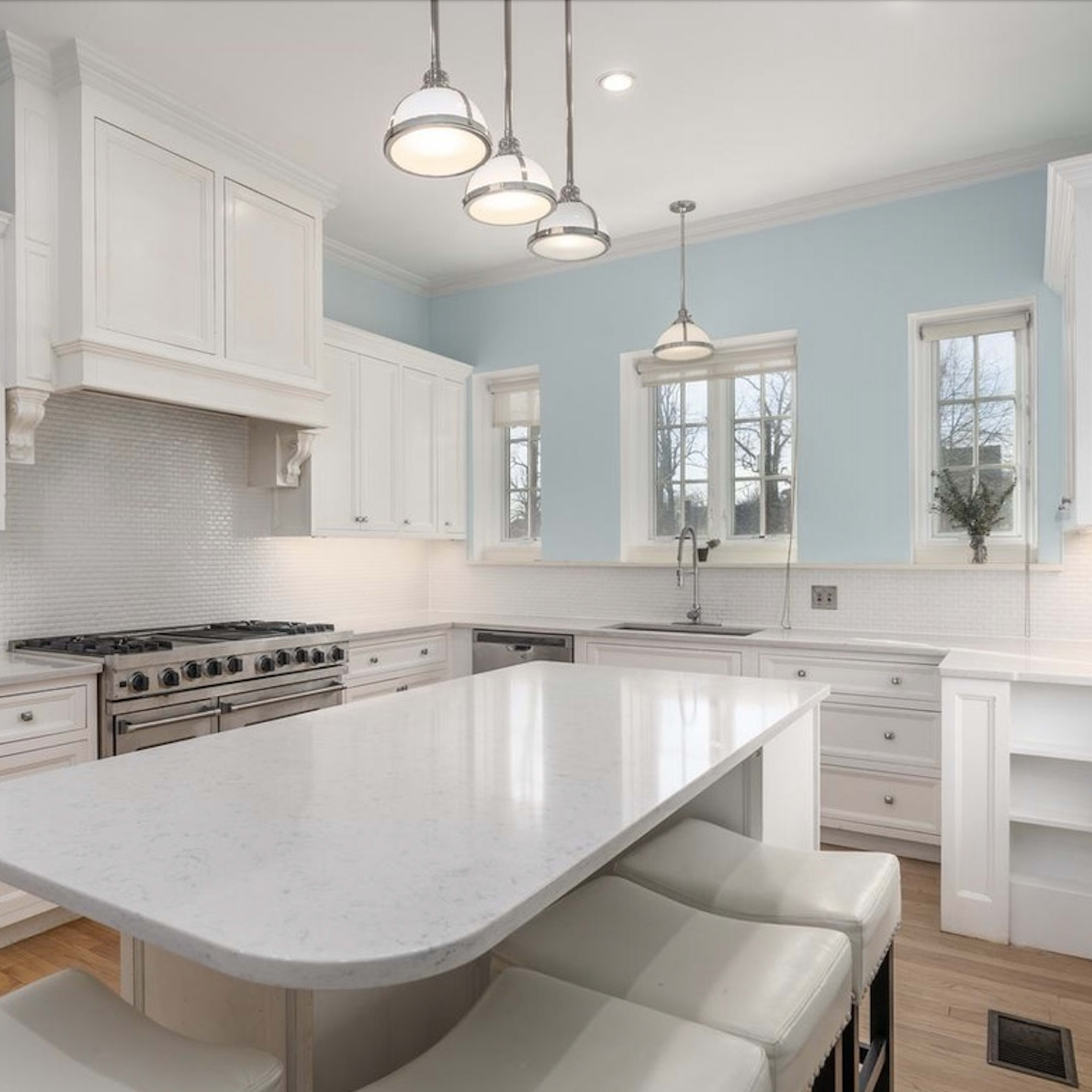A modern kitchen with white cabinetry, a large island with seating, and stainless steel appliances.