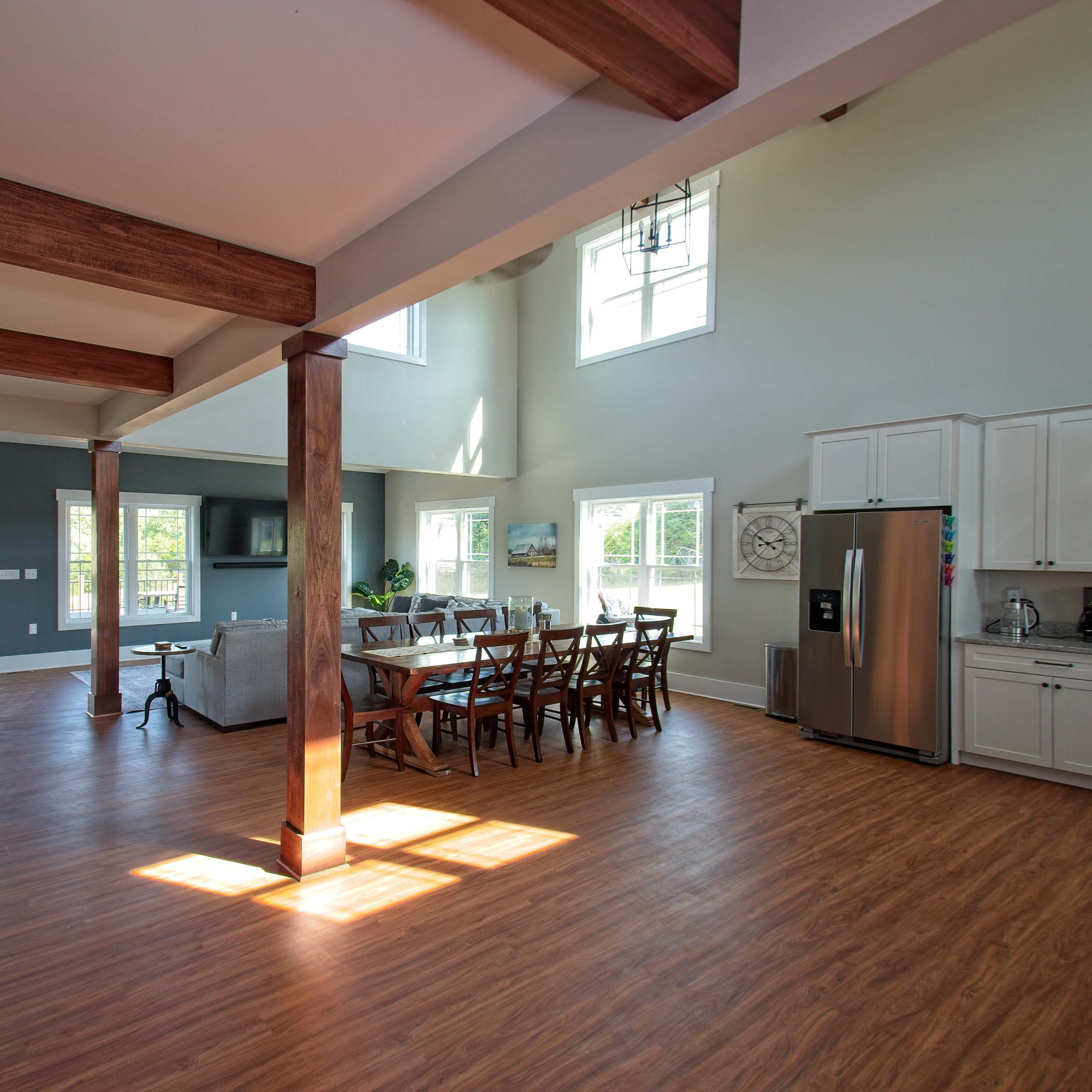 A spacious open-concept living area with wooden beams, large windows, a dining table, and a modern kitchen.