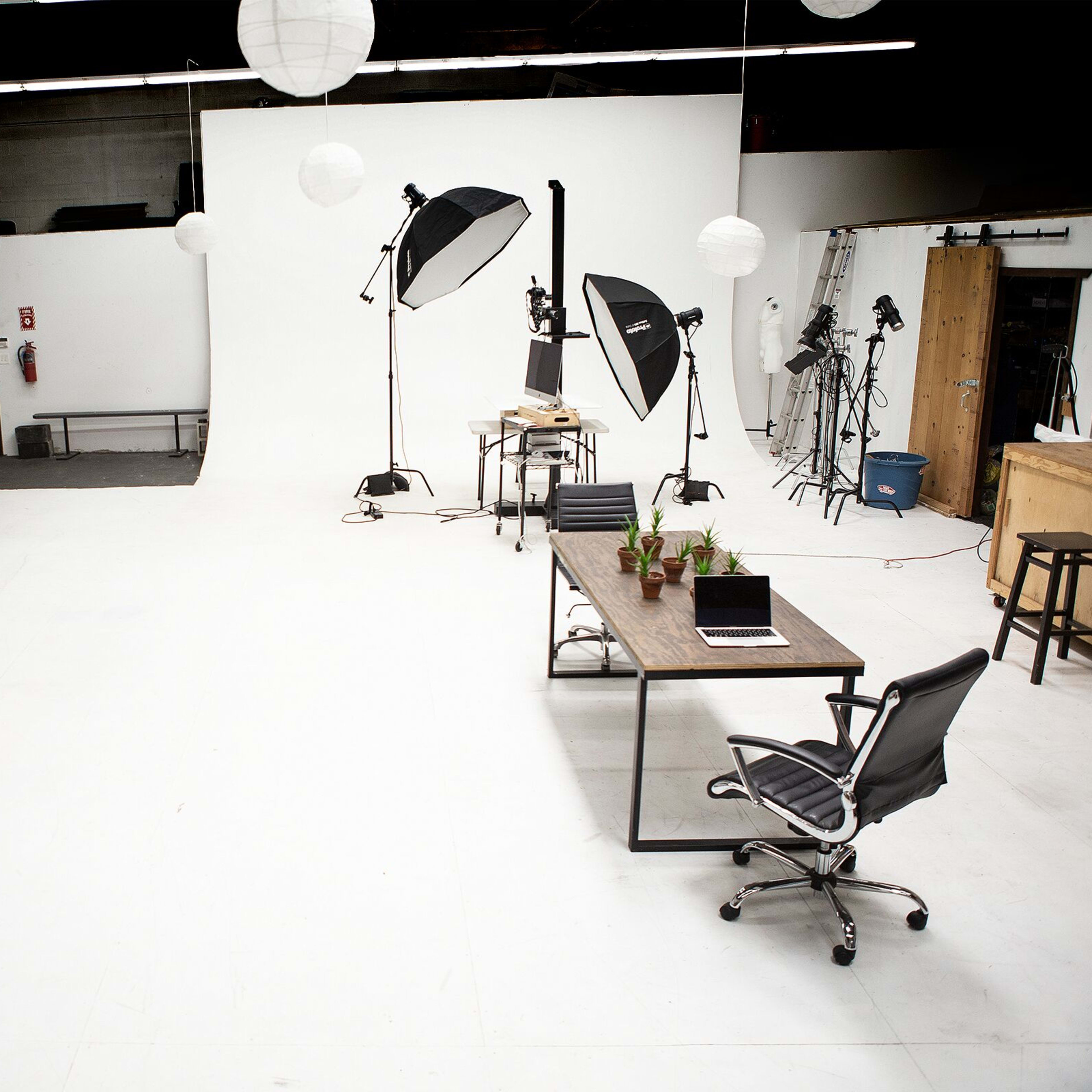 A spacious, well-lit studio with a plain backdrop, multiple photography lights, and a variety of furniture arranged for a photo shoot.