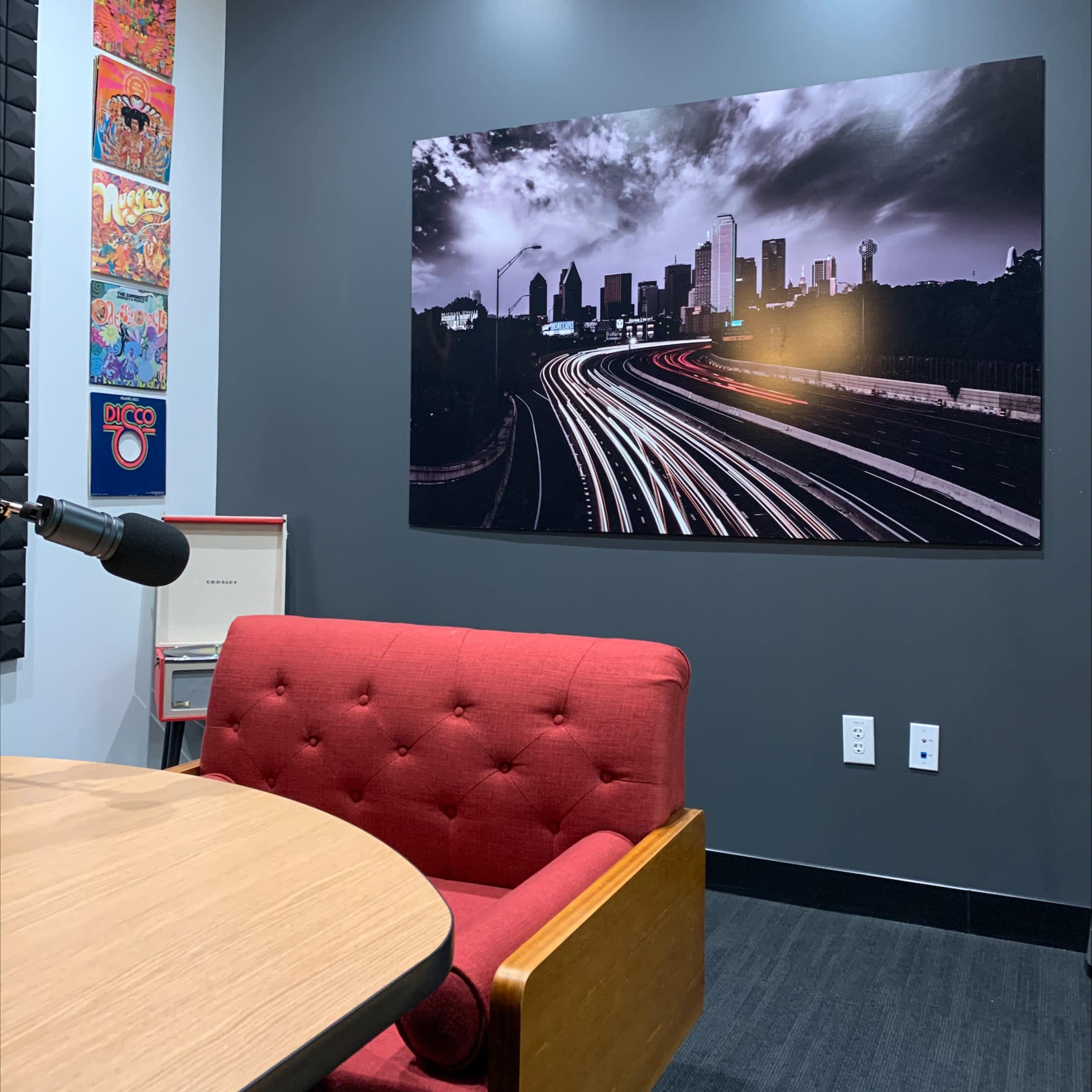 A cozy room with a red tufted chair, a microphone, and a large black-and-white photograph of a cityscape on the wall.