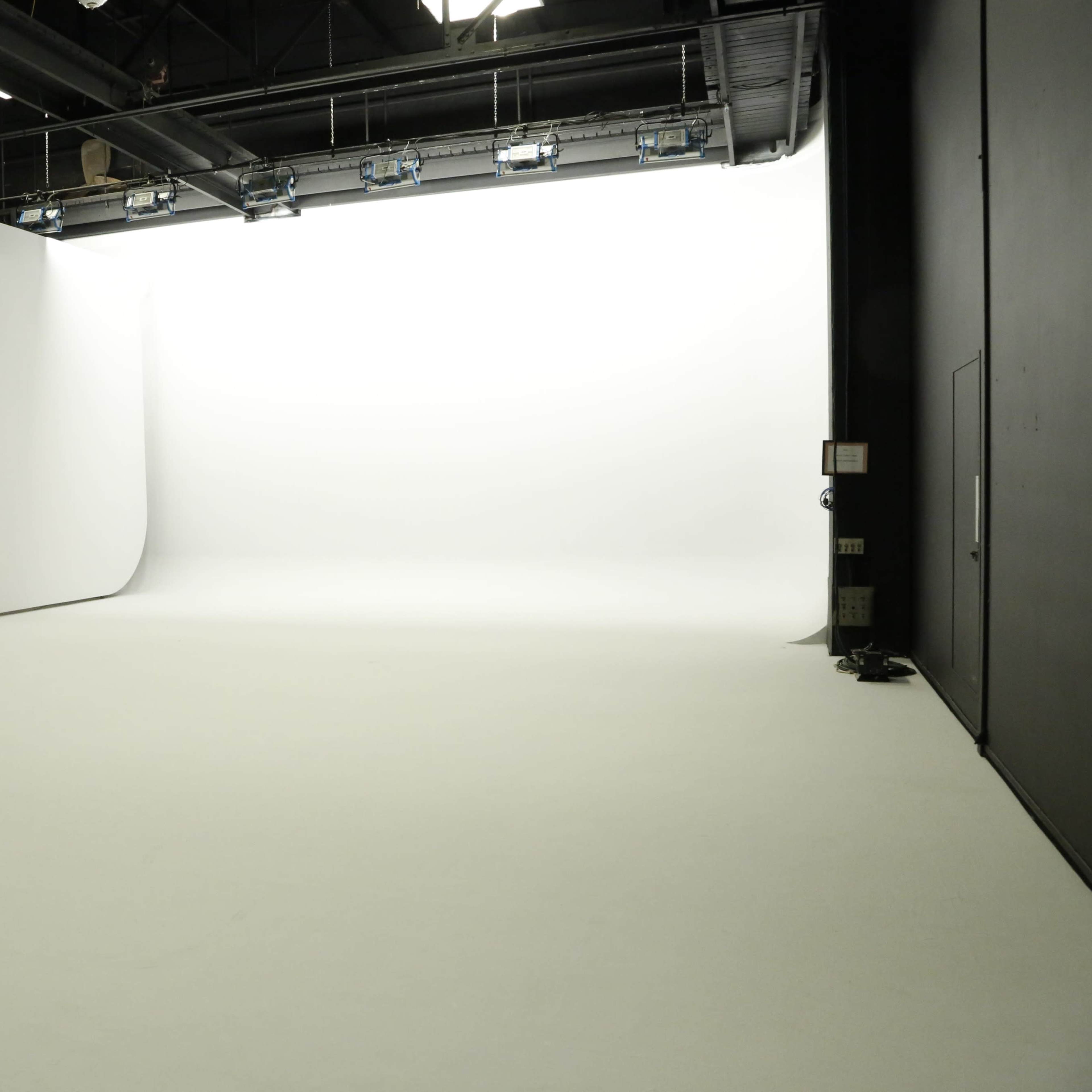 A large, empty photography studio with a seamless white backdrop and a smooth white floor.