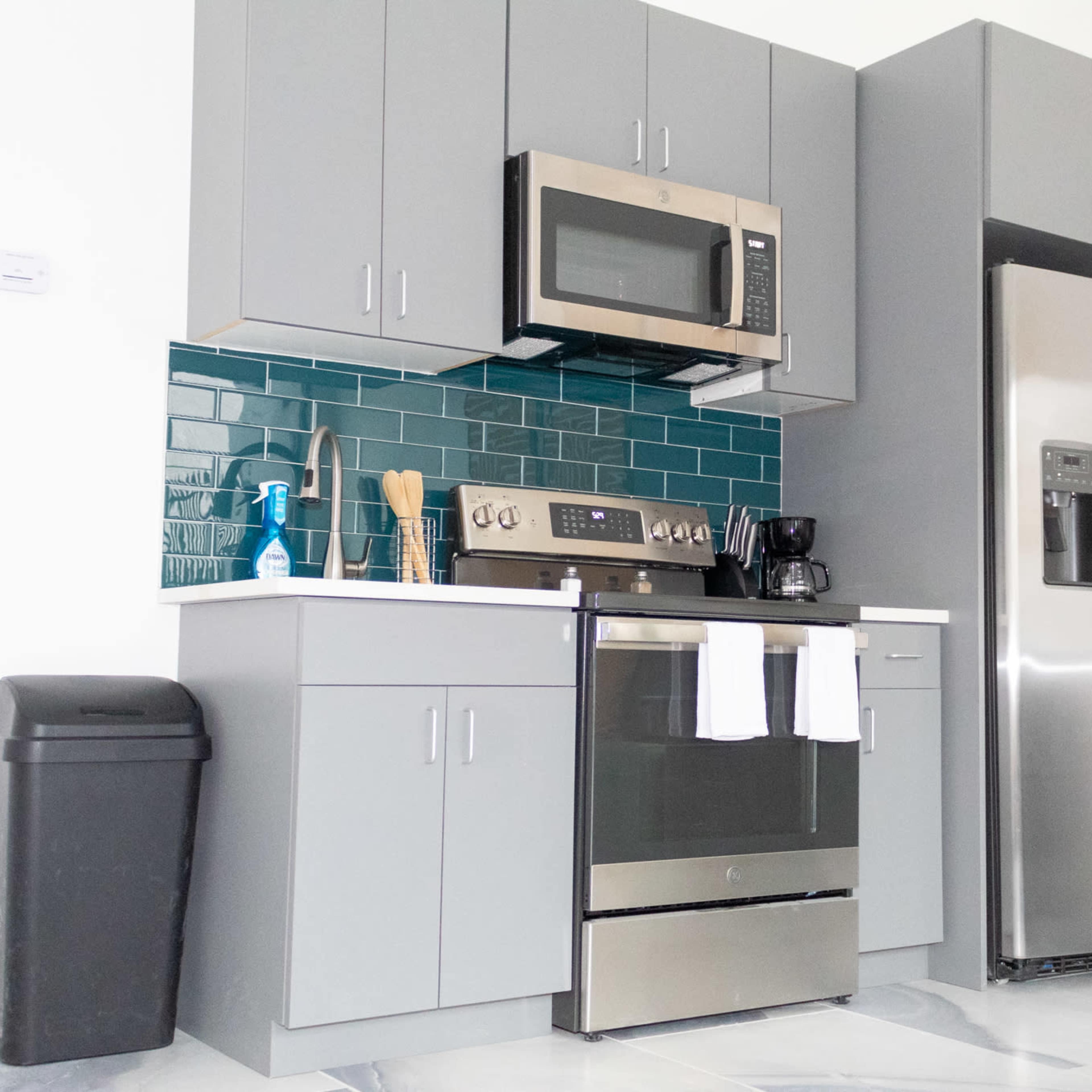 A modern kitchen with gray cabinets, stainless steel appliances, and a teal tiled backsplash.