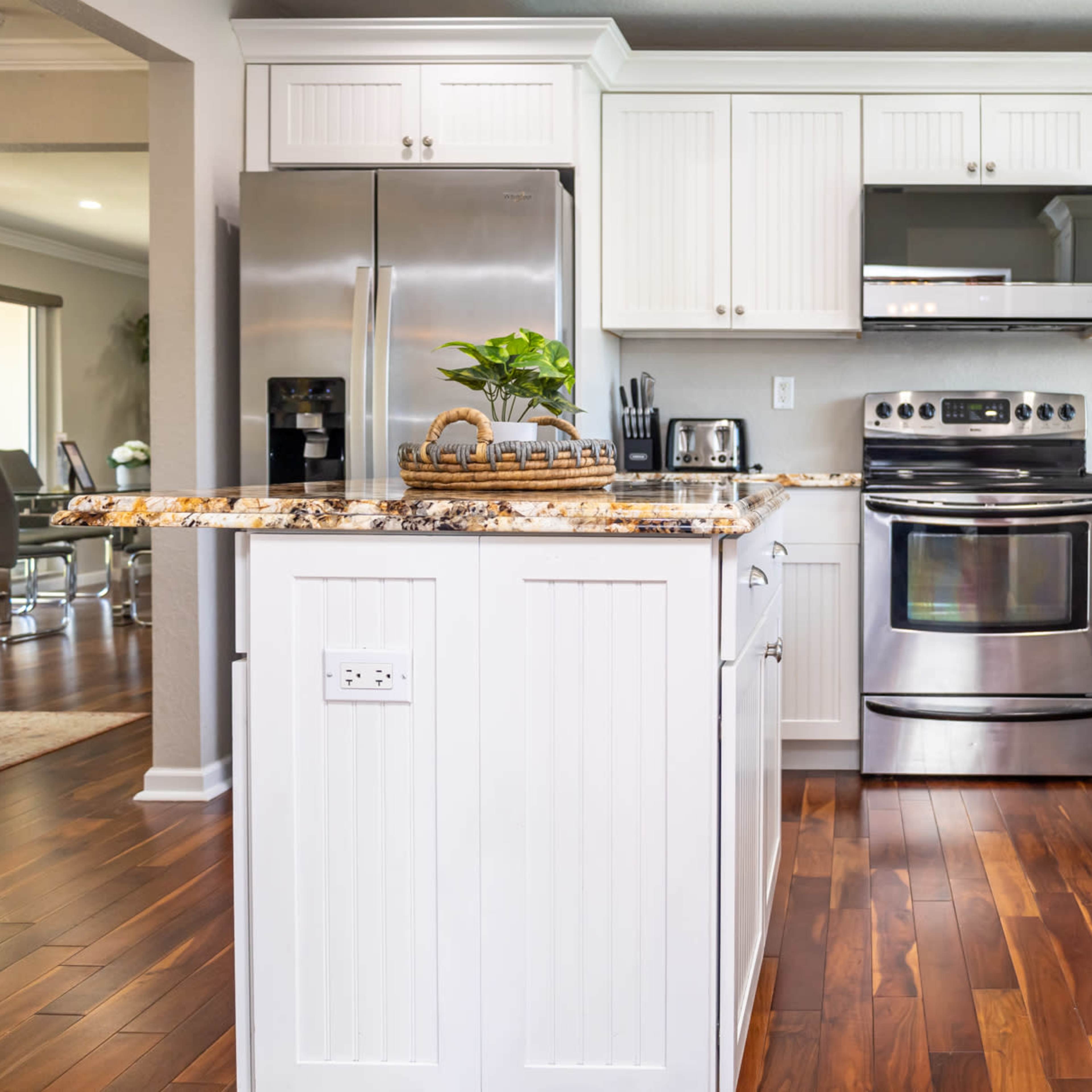The modern kitchen features stainless steel appliances, white cabinetry, and a granite countertop with wood flooring.